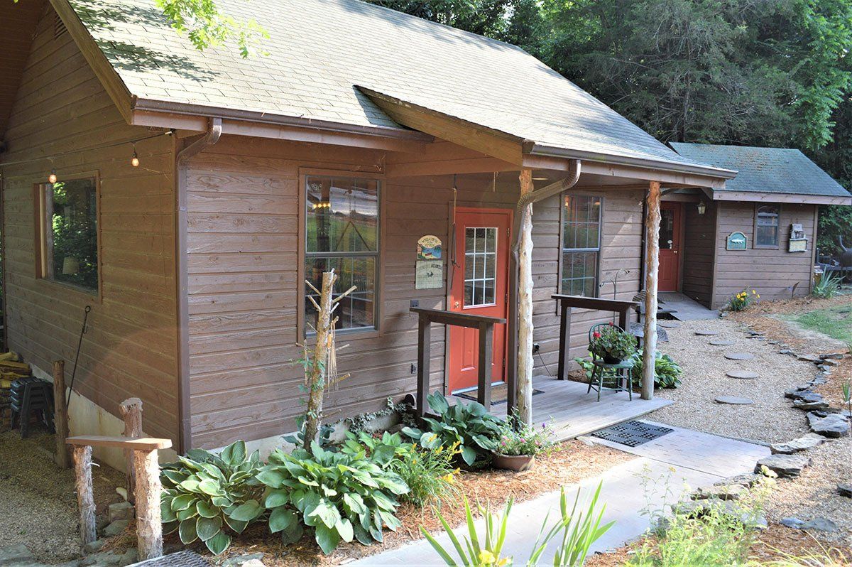 Small rustic cabin with red front door, surrounded by trees and a rocky garden path.
