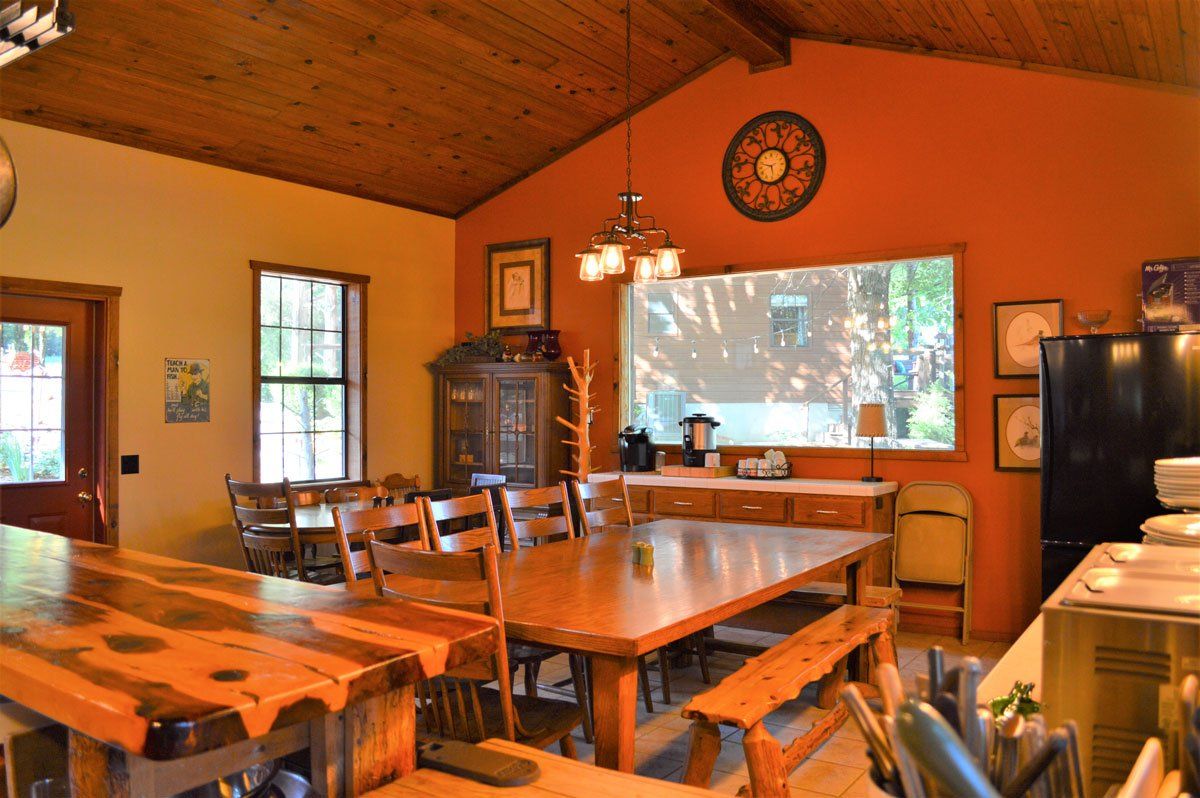 Rustic dining room with wooden tables and chairs, orange walls, and a large projected screen at the front