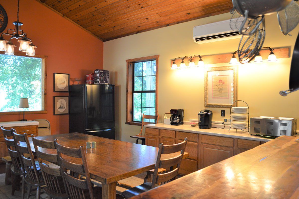 Warm kitchen with long wooden table, bar counter, pendant lights, and stainless steel appliances.