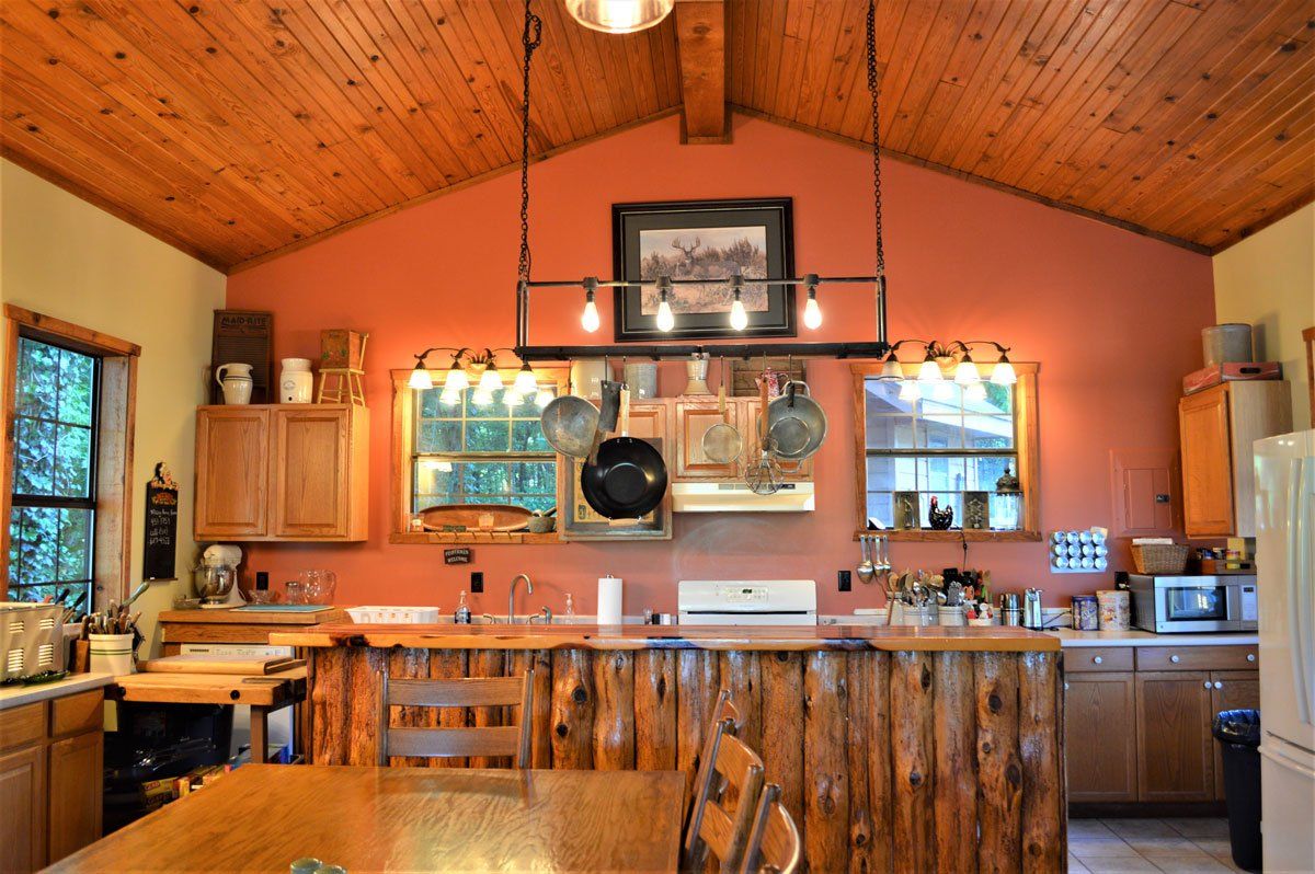 Rustic kitchen with wood ceiling, orange walls, central island, and wood cabinets with hanging utensils.