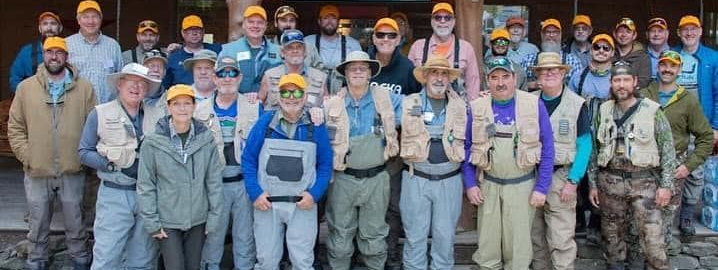 Group of people in work gear and hard hats posing together indoors with a light blue item in front