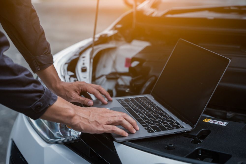 A man is working on a laptop computer under the hood of a car — Locksmith in Tweed Heads, NSW