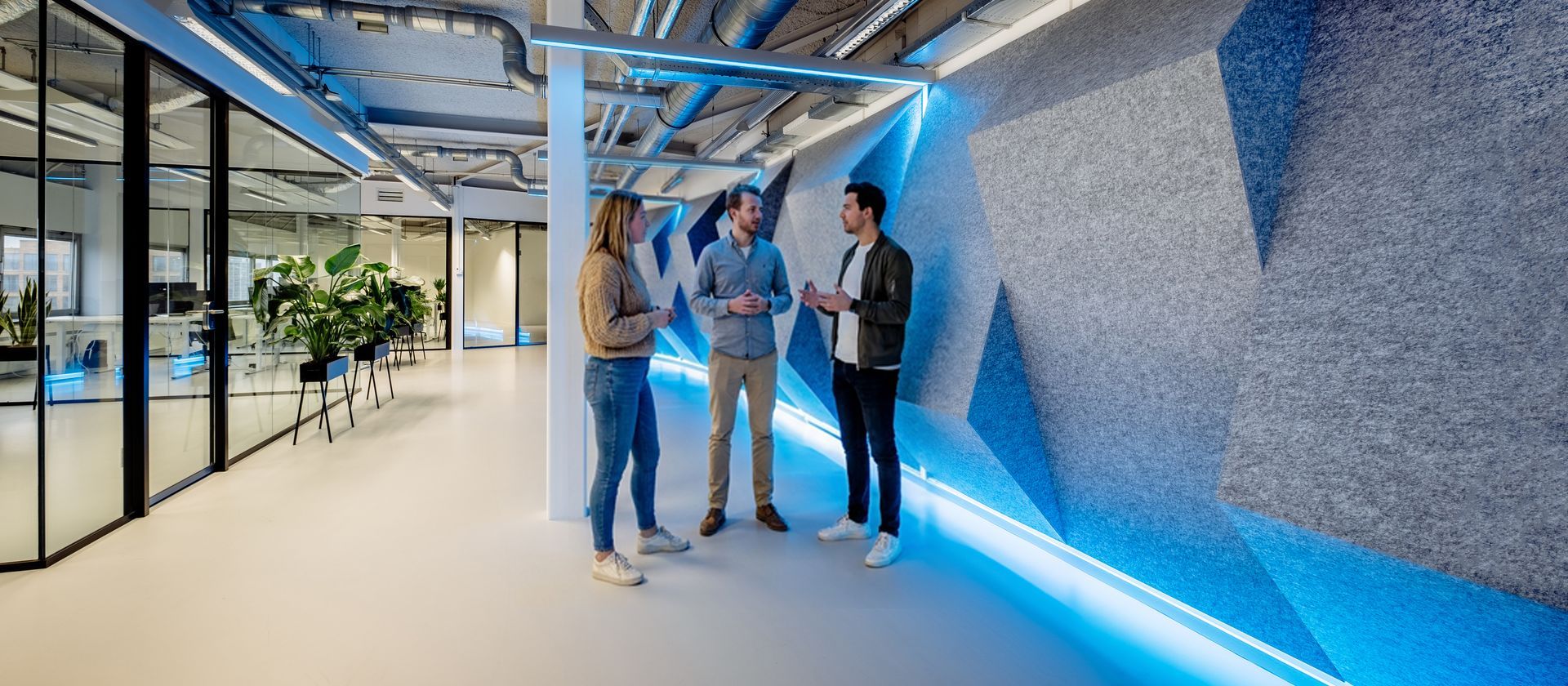 Four people in a bright modern office with blue accent lighting and glass walls. Acoustic elements