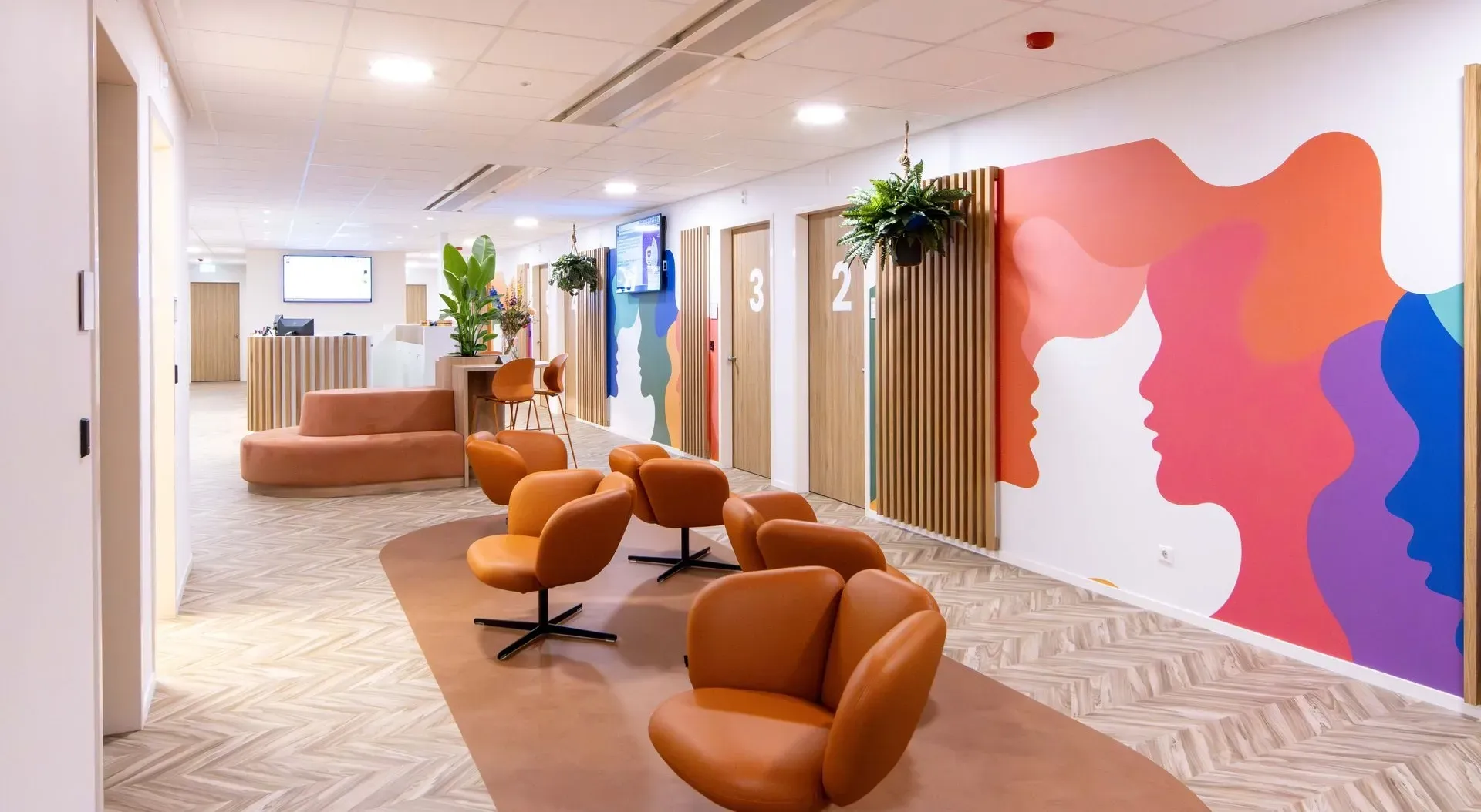 Lichte, moderne kantoorhal met oranje loungestoelen, planten en een kleurrijke abstracte muurschildering.