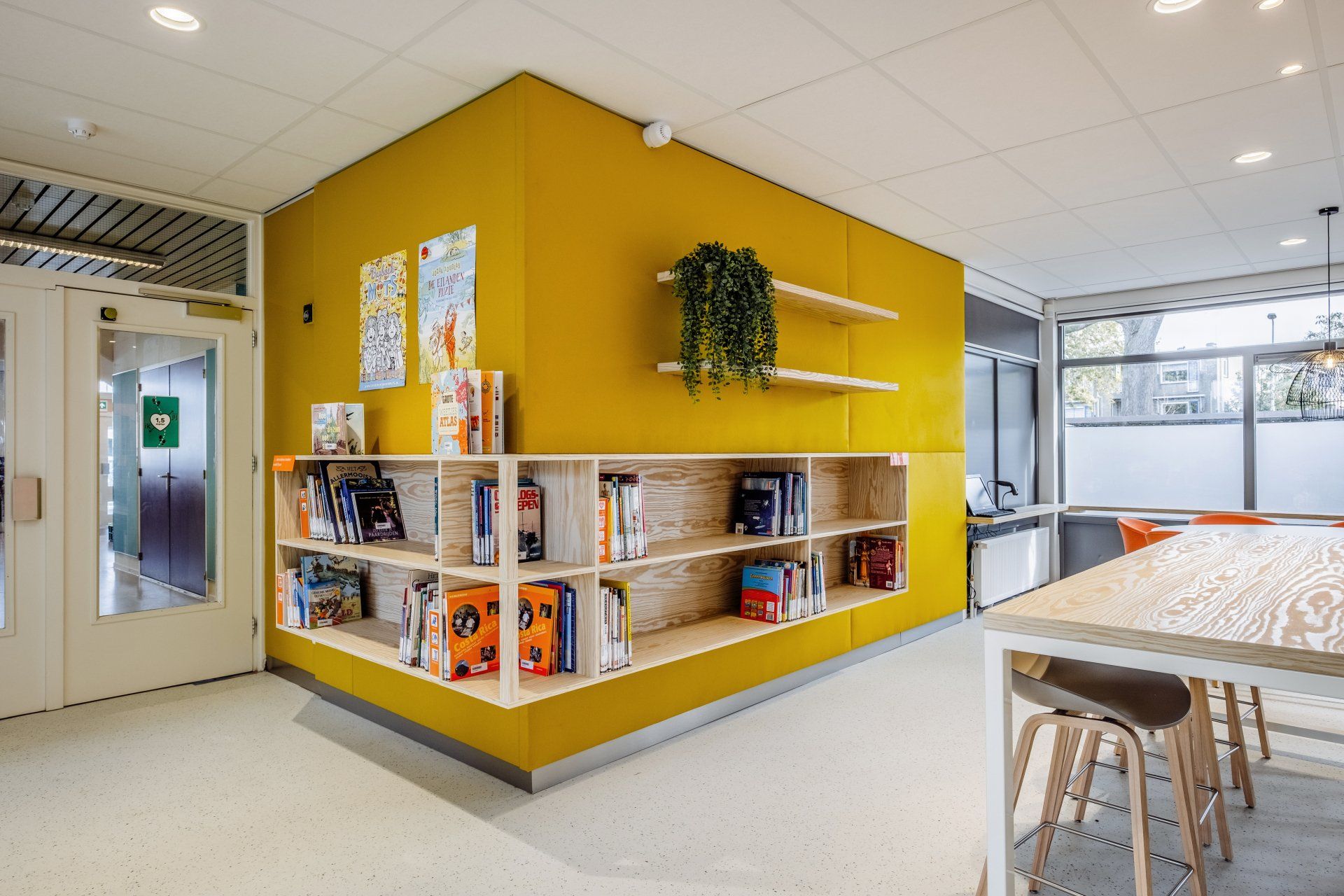 Een moderne wachtkamer van een medische praktijk met oranje stoelen, houten deuren en een kleurrijke abstracte muurschildering van gezichten in het nieuwe kantoor van GGD Haaglanden in Den Haag, interieurontwerp door KuóStudio