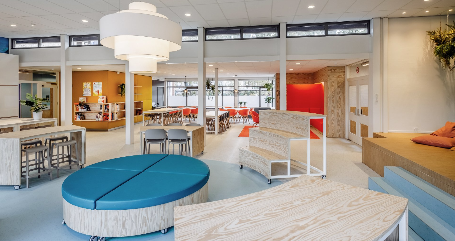 Moderne, open lounge met blauw-witte zitmeubels, tafels, grote ramen en kleurrijke muuraccenten.