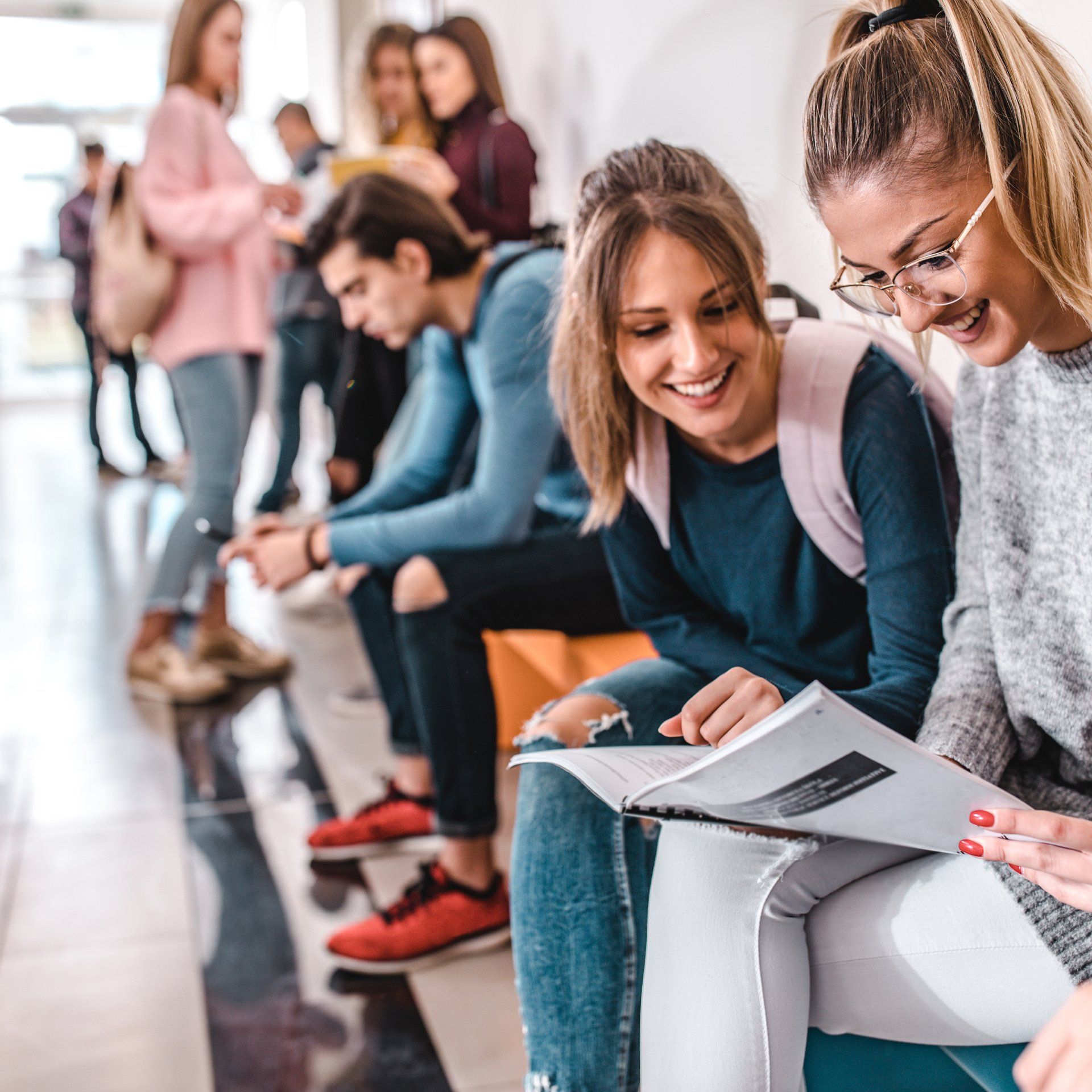 Twee lachende studenten bekijken samen een document in een lichte zaal, terwijl op de achtergrond andere mensen staan en zitten. Oplevering Interieurontwerp
