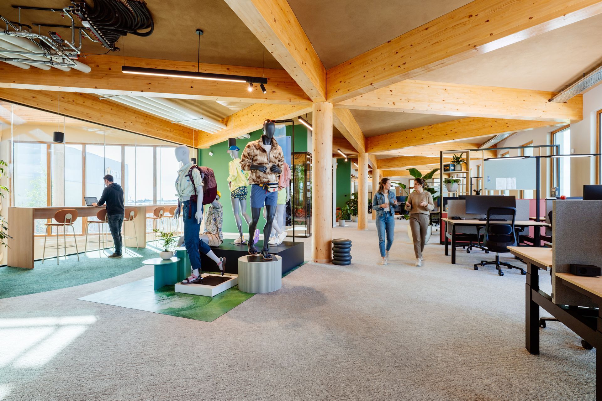 Open kantoorlounge met mensen die bij tafels staan ​​en een plafond met houten balken. Bever