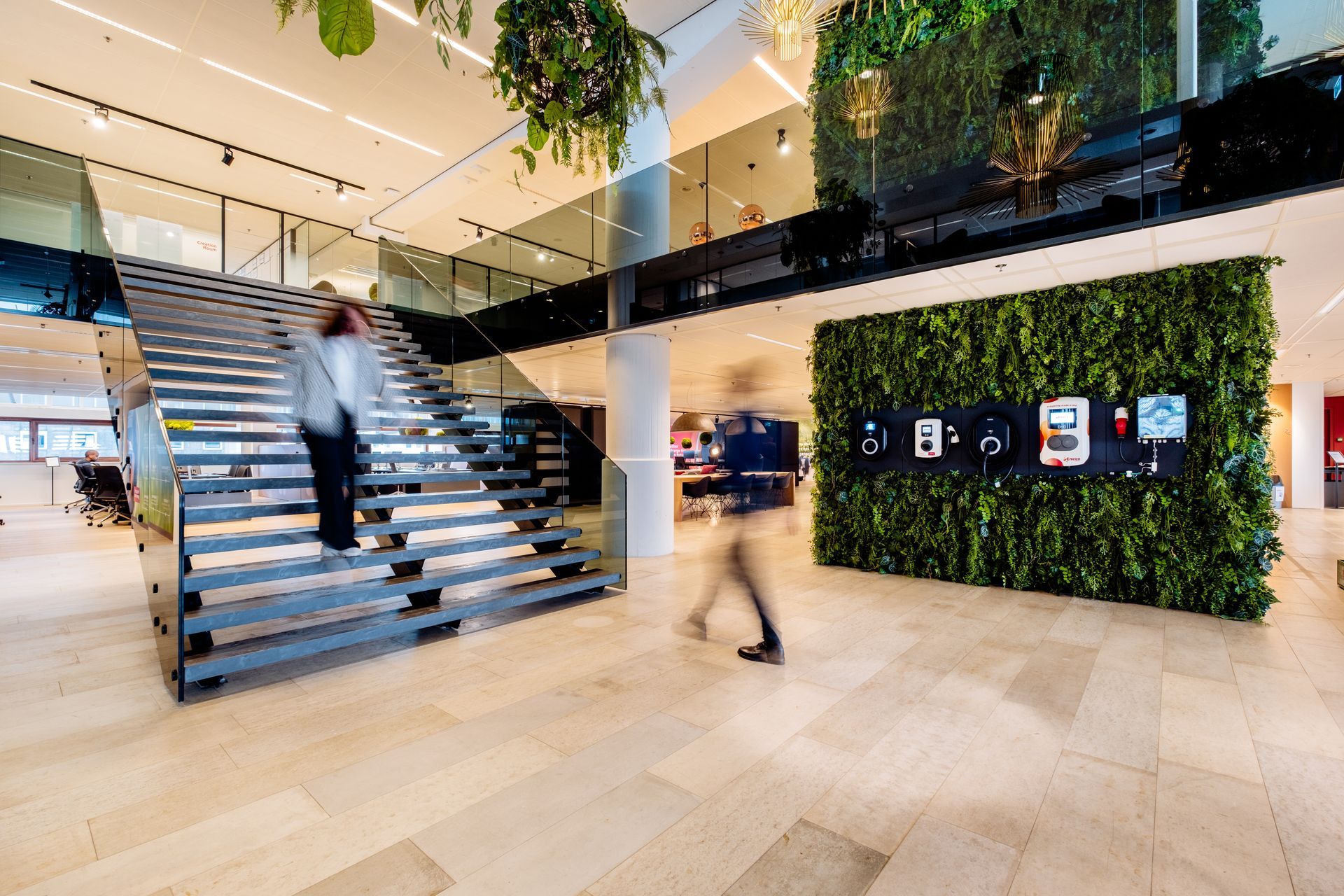 Moderne kantoor lobby met brede trappen, een groene wand en mensen die door een licht atrium lopen.