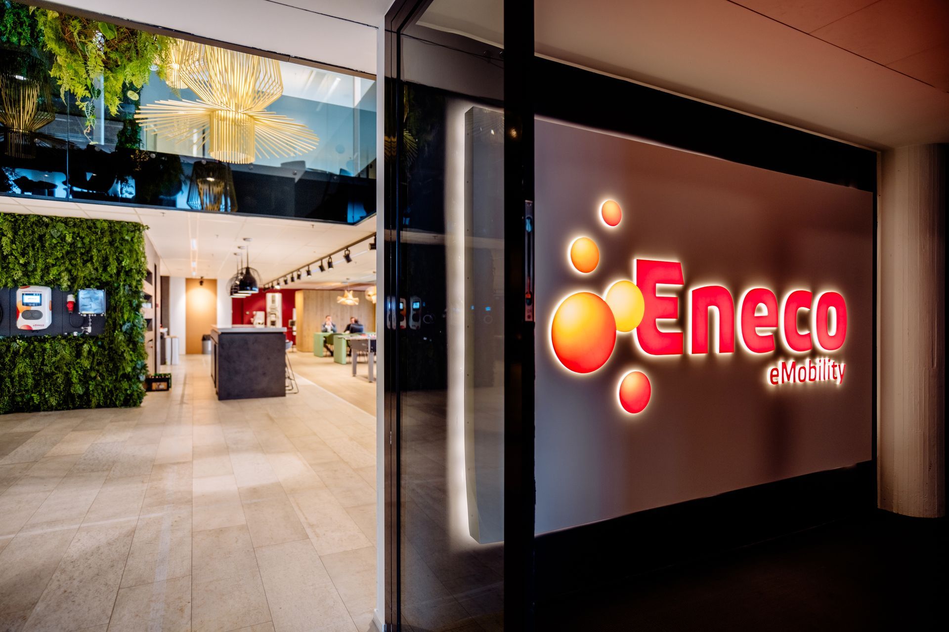 Het Eneco-logo naast een open deuropening toont een modern kantoorinterieur. Interieurontwerp KuóStudio van het kantoor Rotterdam Eneco eMobility