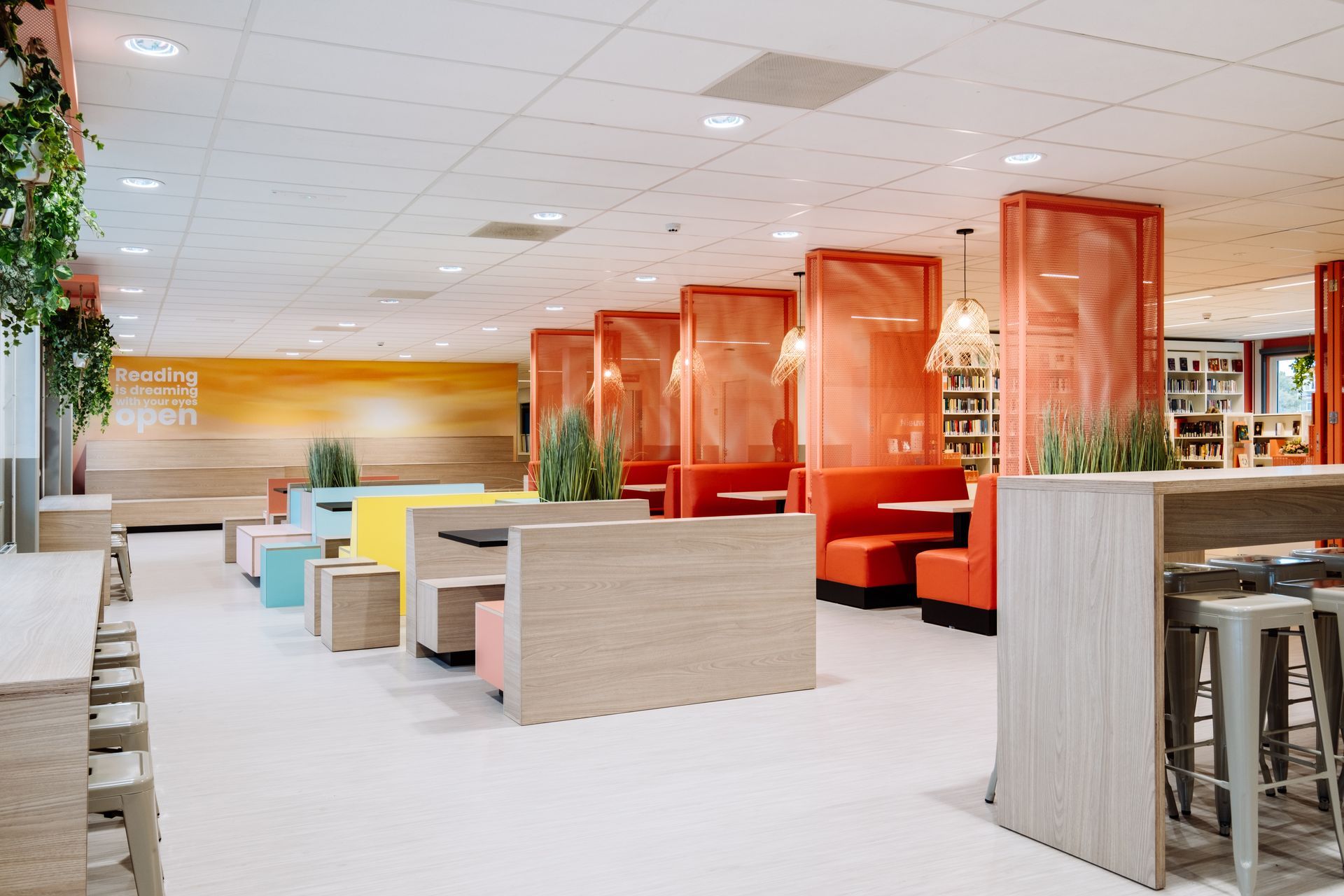 Iemand loopt door een lichte kantoorlobby met hangplanten, gouden hanglampen en een houten trap in het nieuwe kantoor van Eneco eMobility in Rotterdam, interieurontwerp door KuóStudio
