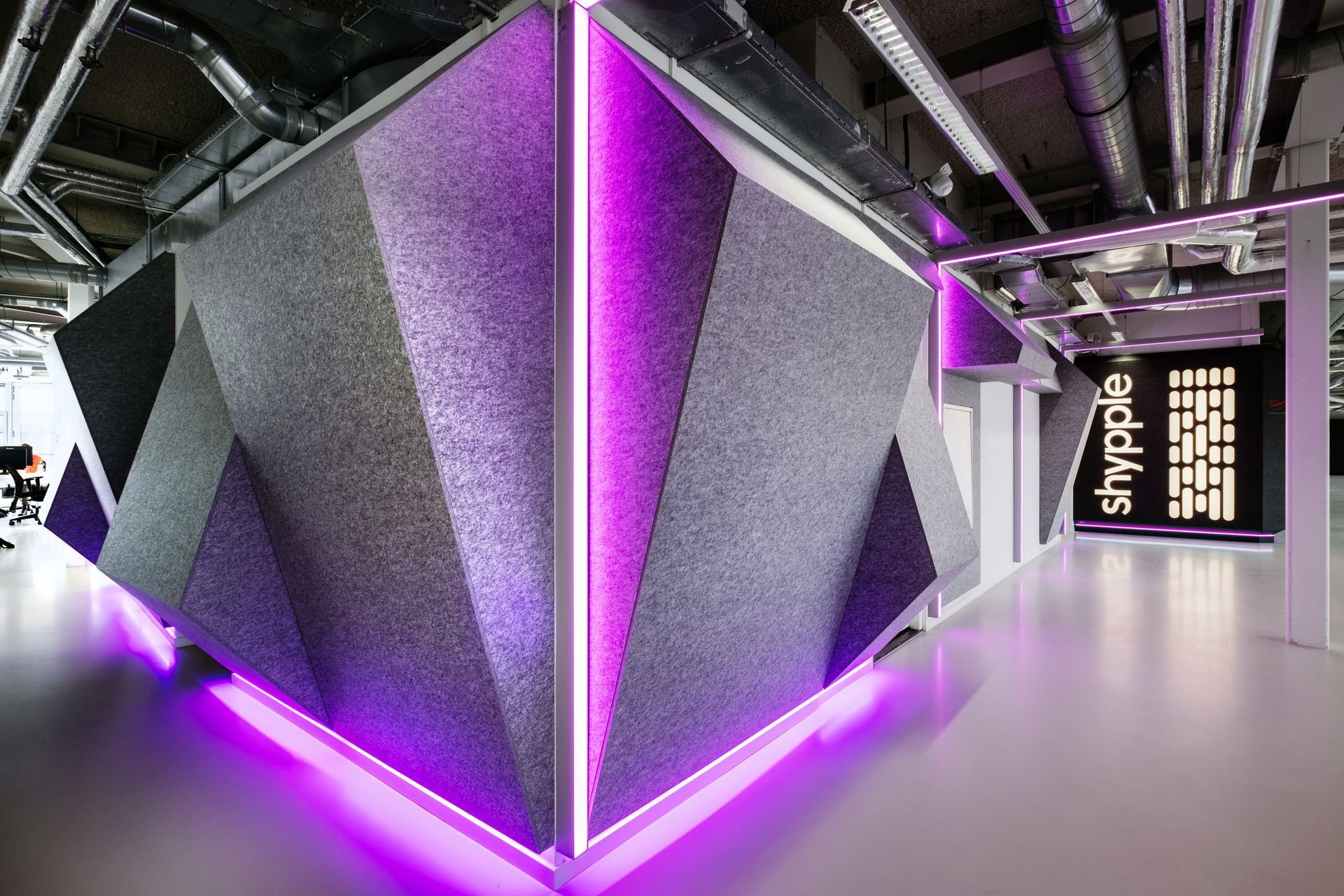 Een moderne kantoorhoek met gestructureerde, geometrische akoestische wandpanelen, geaccentueerd door felpaarse ledstrips in het nieuwe kantoor van Shypple in Rotterdam, interieurontwerp voor KuóStudio