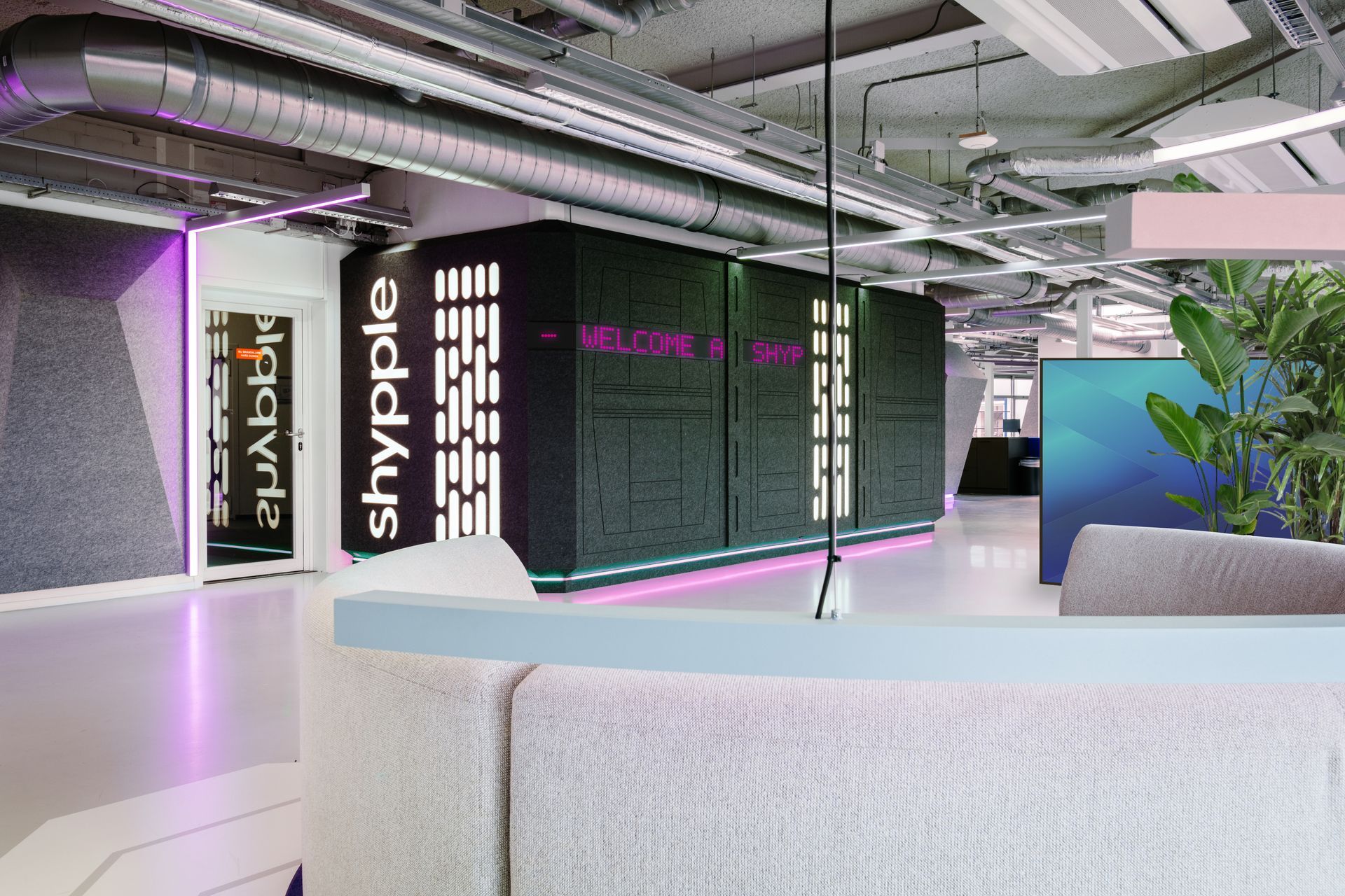 Moderne kantoorlobby met paarse, sfeervolle verlichting, witte zitmeubels en een groene plantenarrangement.