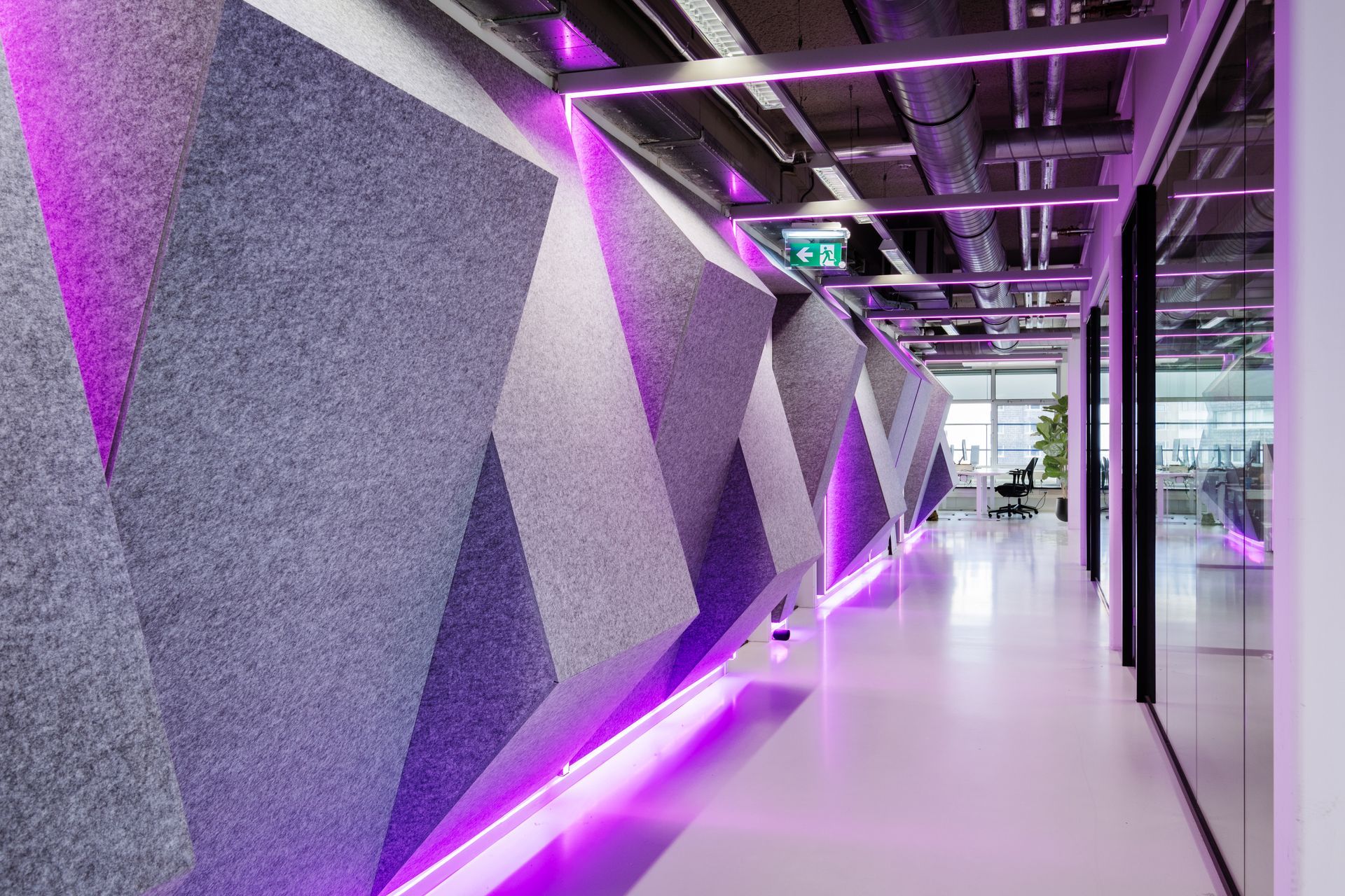 Een gang met futoristische geometrische, akoestische wandpanelen, verlicht door felpaarse ledstrips in het nieuwe kantoor van Shypple in Rotterdam, interieurontwerp voor KuóStudio