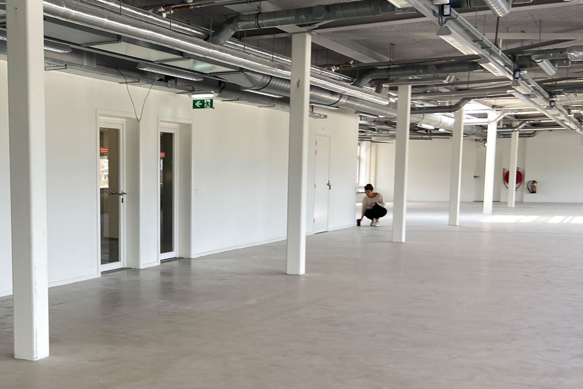 Voor verbouwing: Een leeg kantoor met witte muren, betonnen vloeren, zichtbare plafondleidingen in het kantoor van Shypple in Rotterdam.