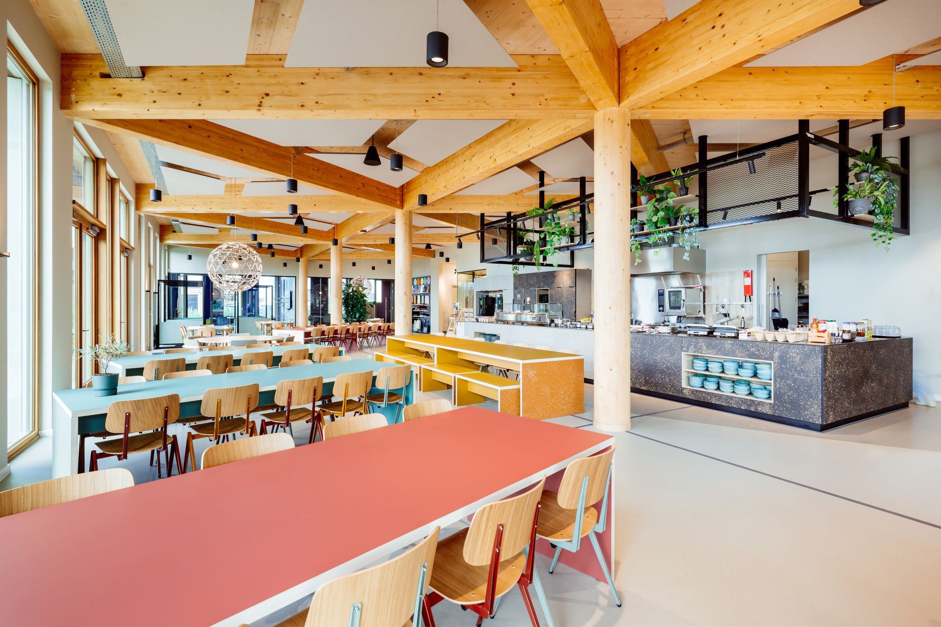 Modernelunchruimte met zichtbare houten balken, lichte houten tafels en stoelen, en een serveerbalie met stenen blad  in het nieuwe kantoor van Bever, interieurontwerp door KuóStudio