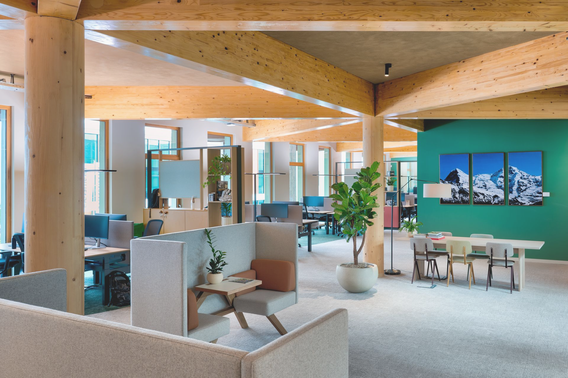Moderne lounge met houten balken, grijze zitmeubels, planten en een eethoek in een licht kantoorinterieur.