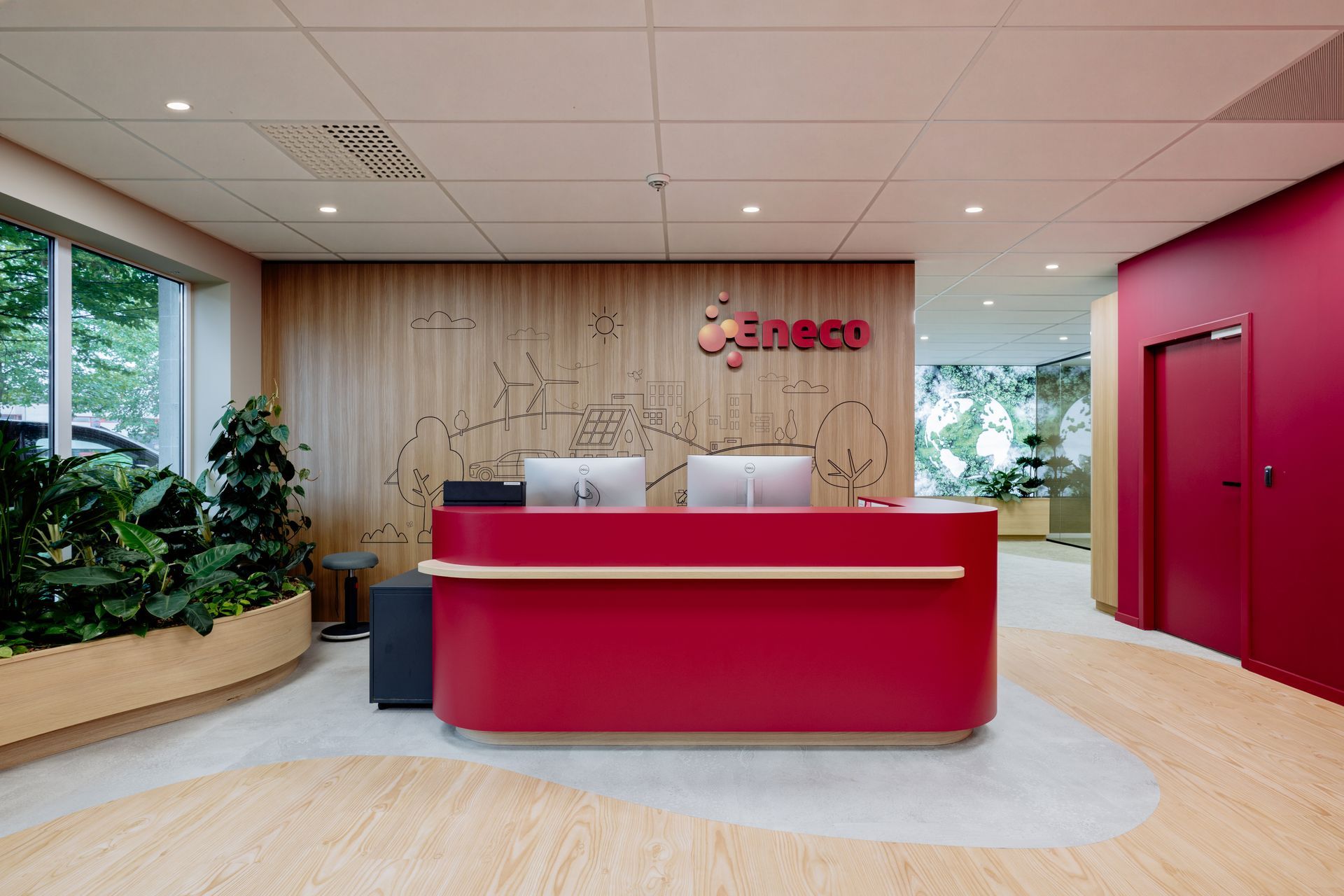 Moderne lounge met gebogen rode zitmeubels, ronde poefs, planten en grote ramen in een lichte kantoorlobby.