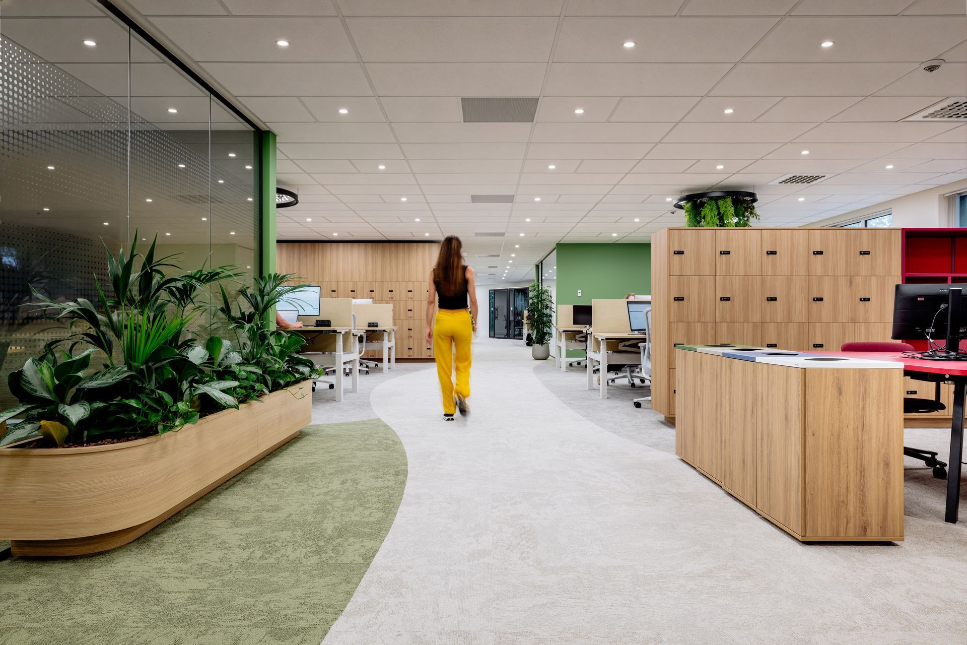 Open kantoorruimte van Eneco Belgium met houten bureaus, computermonitoren en hangende groene planten onder heldere plafondlampen.