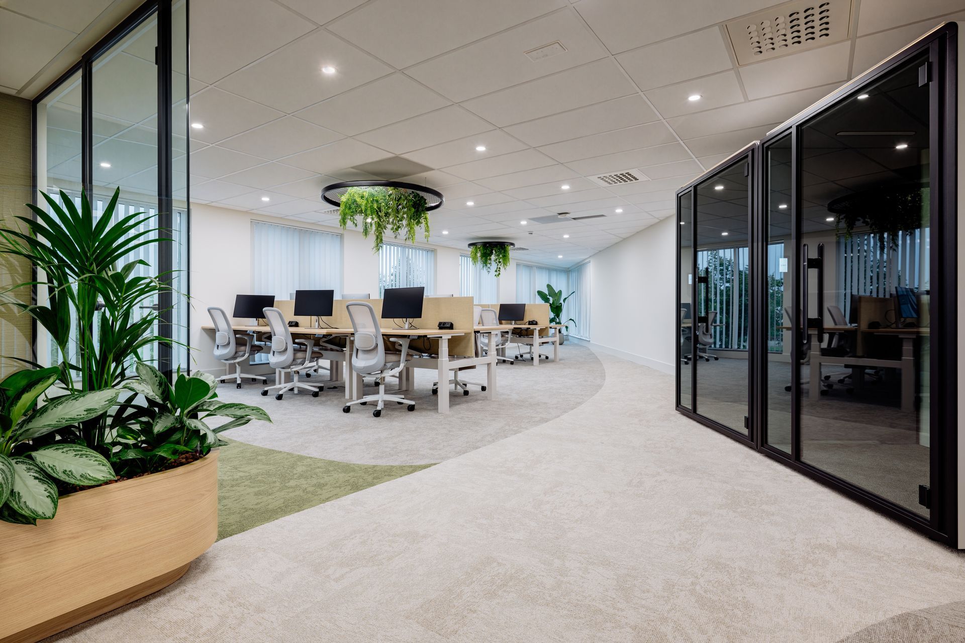 Moderne kantoorlounge met vergadertafels, glazen wanden en grote potplanten. Biophilic Design