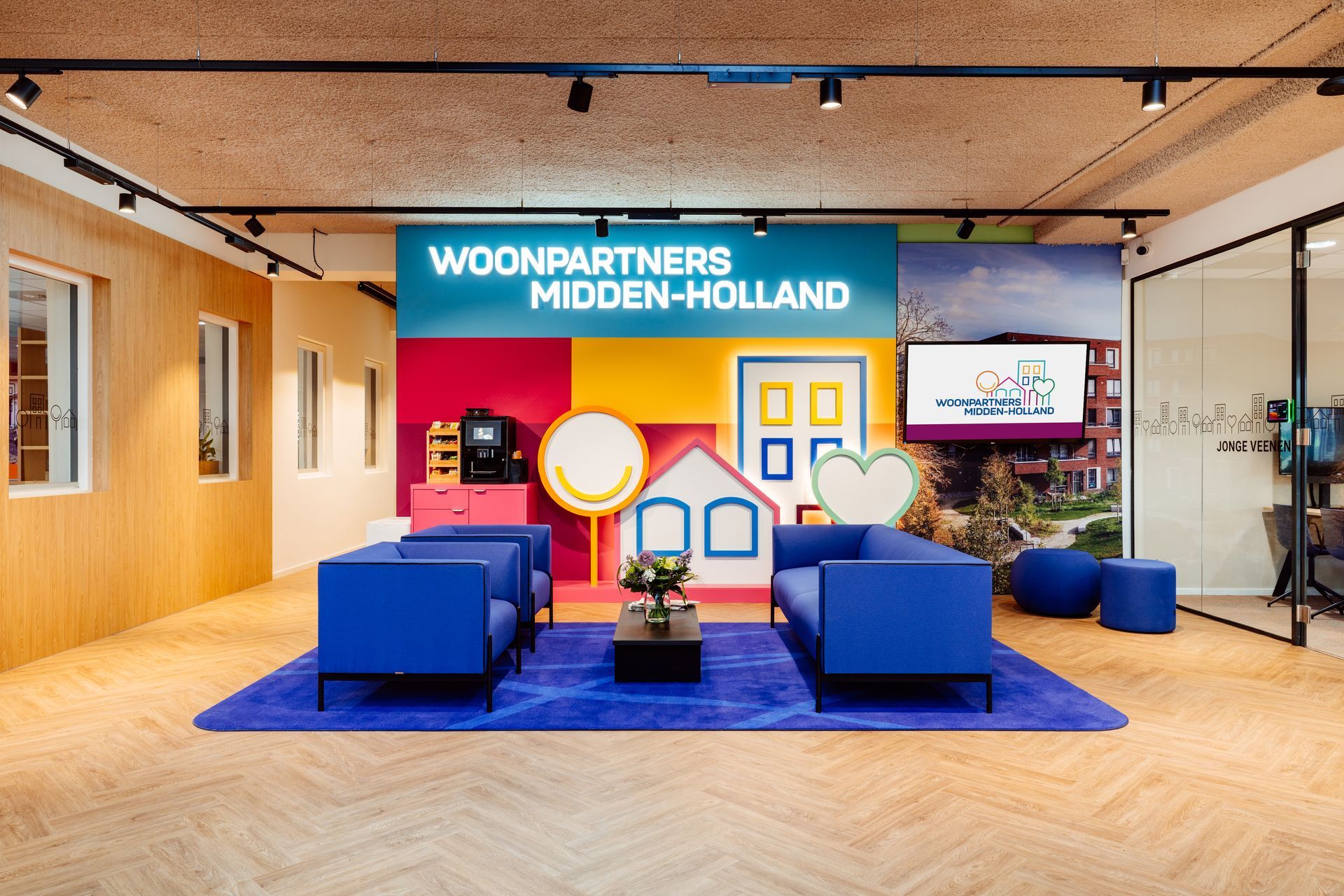 Kantoor entree met blauwe zitmeubels, een kleurrijke achtergrond in de vorm van een huis en een bord met de tekst 