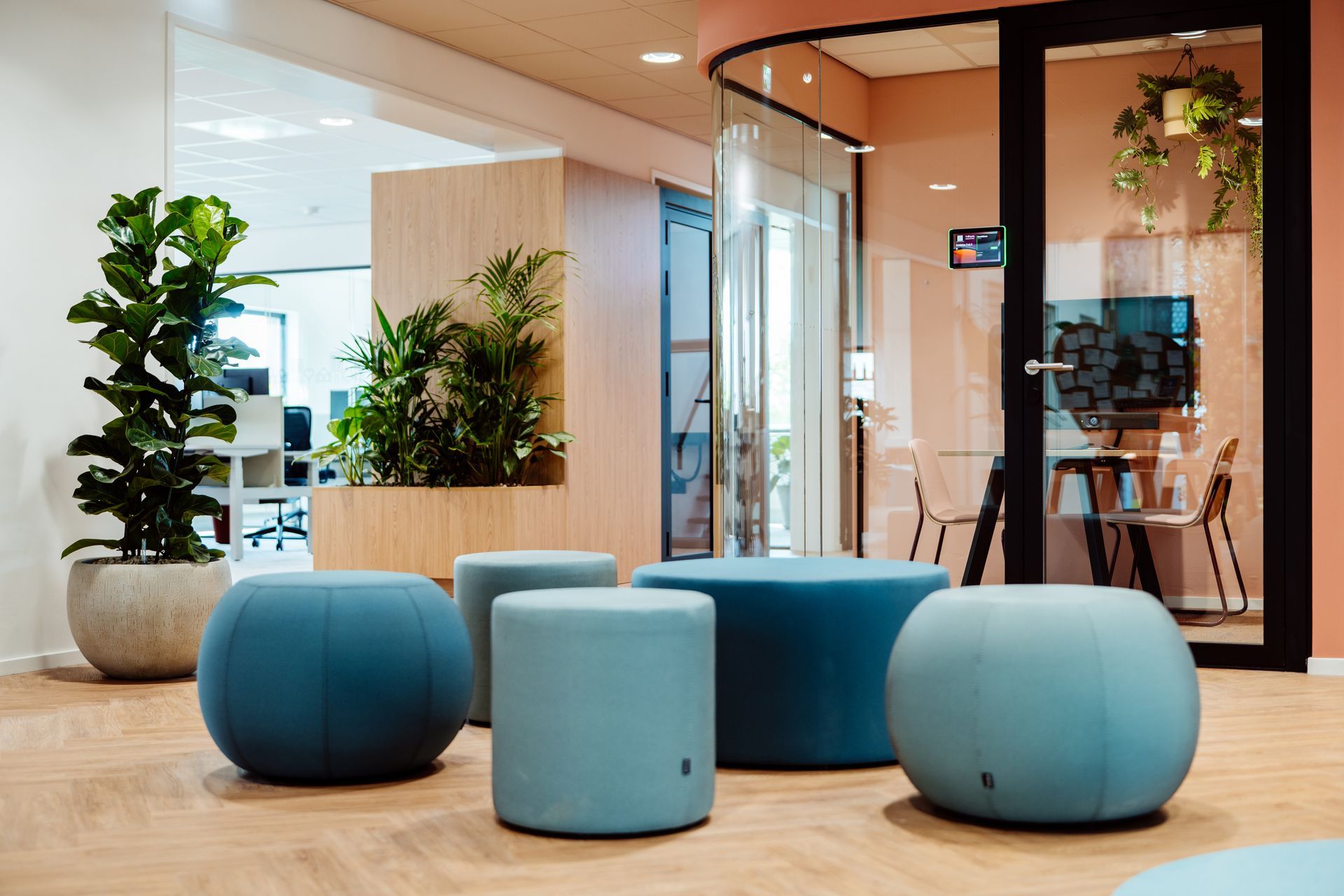 Moderne kantoorlounge met blauwe krukken, potplanten en een vergaderruimte met glazen wanden.