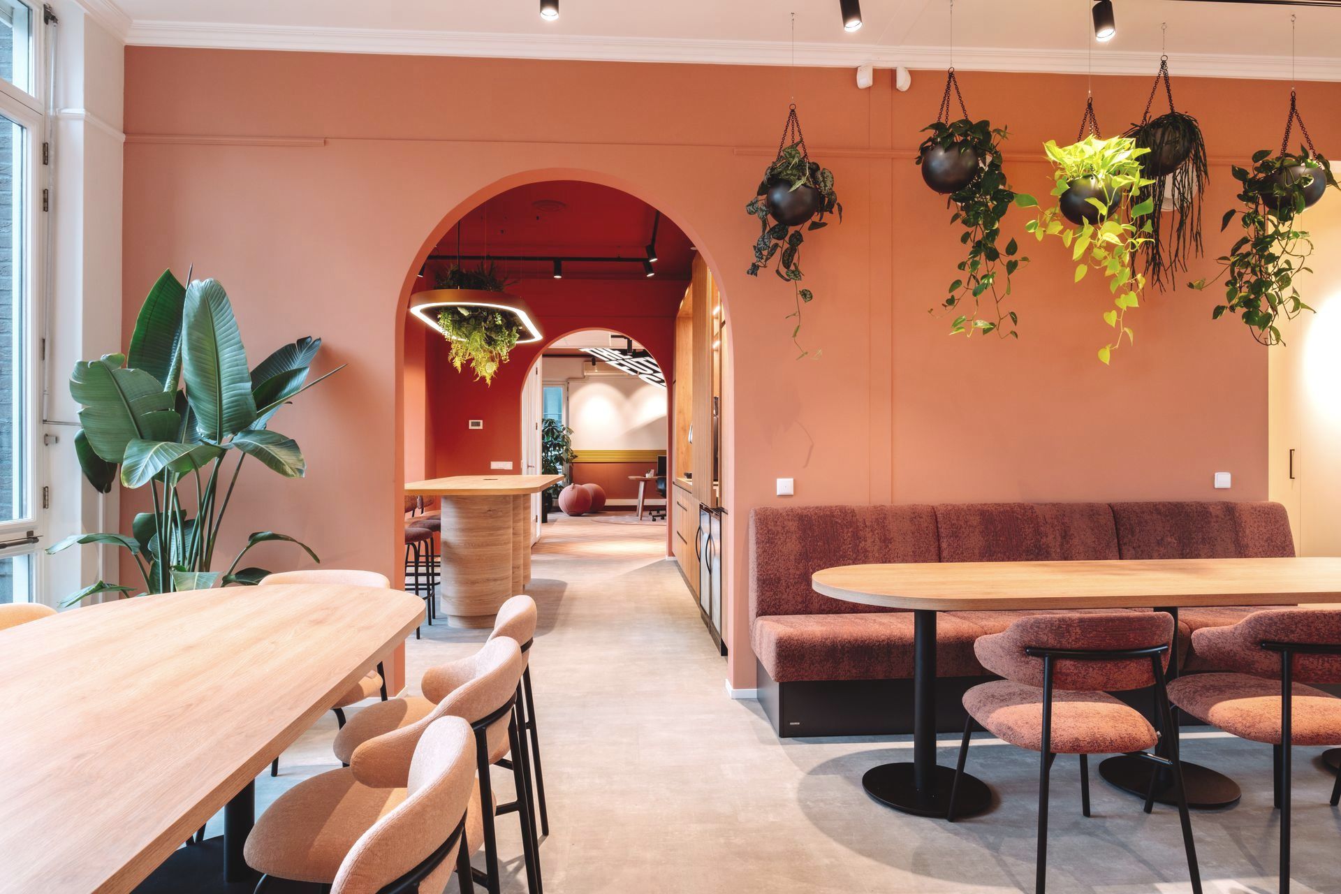 Een moderne, terracottakleurige lounge met een gewelfde doorgang, hangplanten, houten tafels en comfortabele zitkussens in het nieuwe kantoor van The Future Group Interieurontwerp KuóStudio