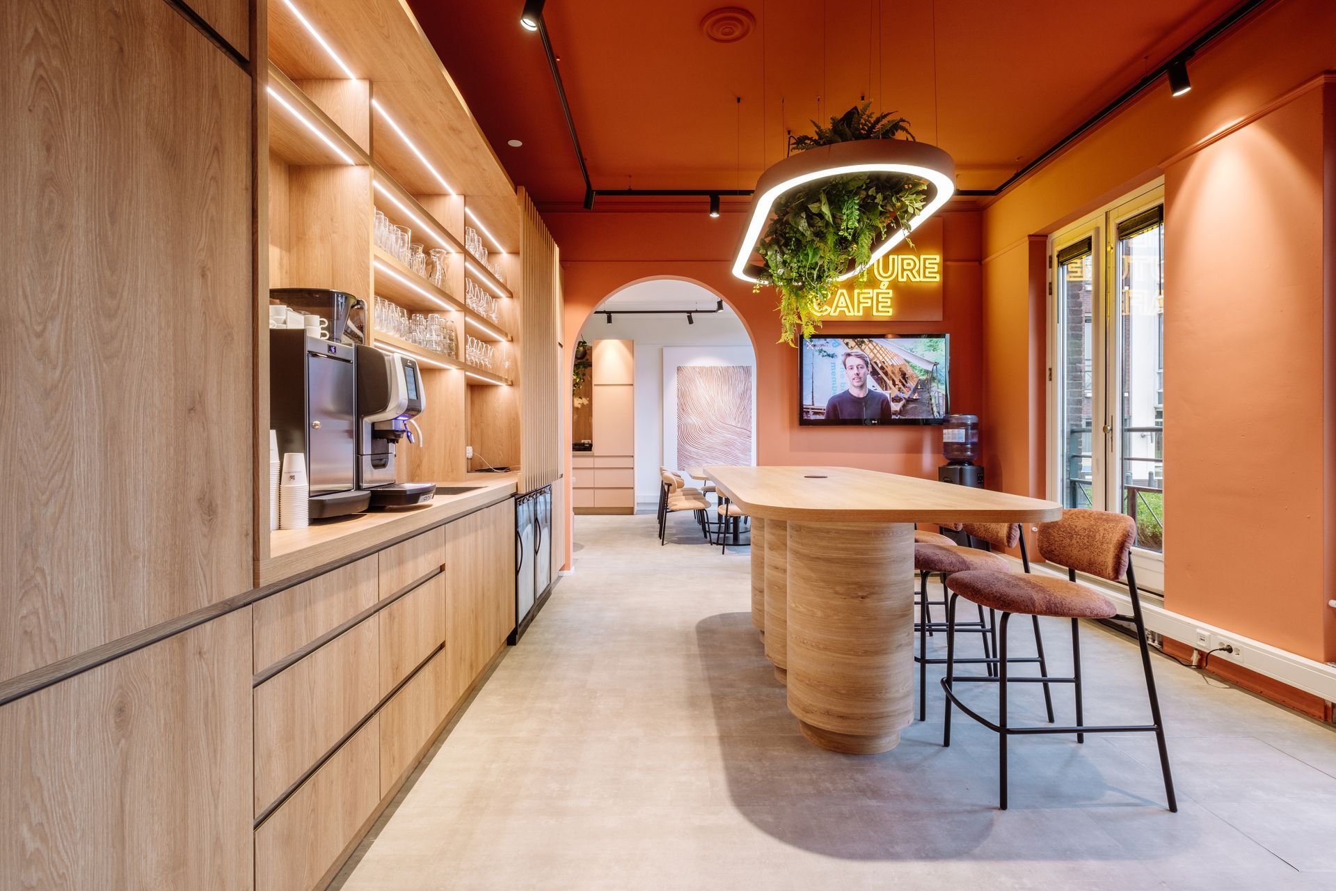 Moderne keuken met terracotta muren, houten kasten, een kookeiland, barkrukken en een hangende plantenlamp in het nieuwe kantoor van The Future Group