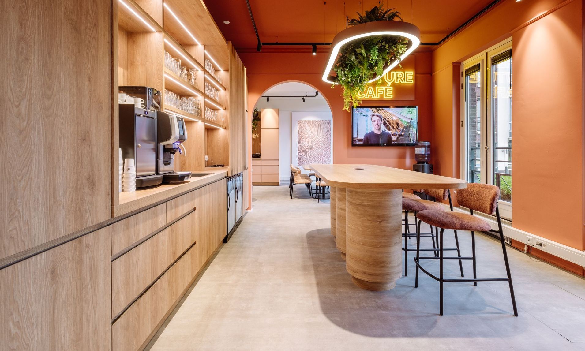 Warme oranje hal met houten kasten, een bar, barkrukken en uitzicht op een lichte kamer in kantoor in Zoetermeer