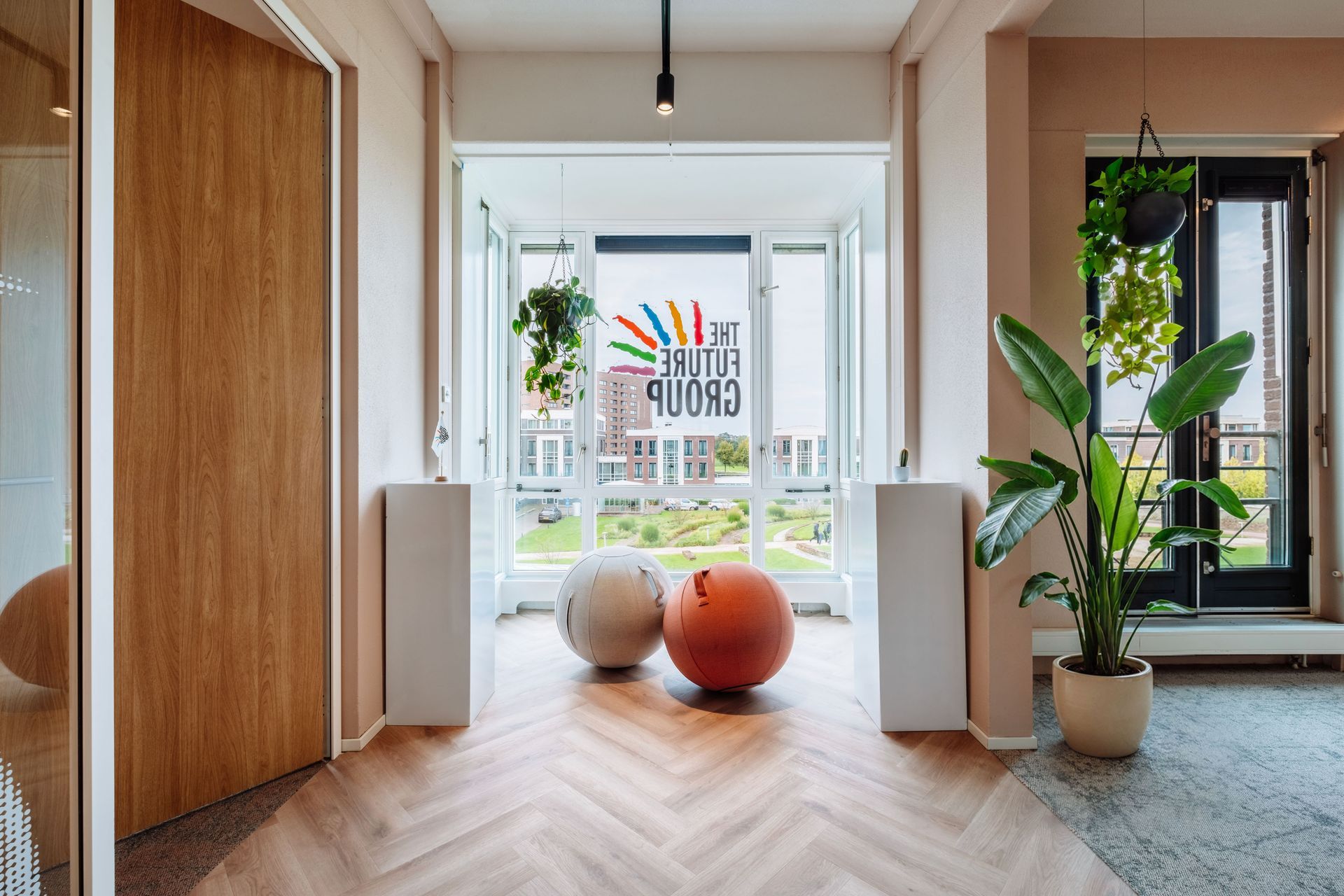 Bright hallway with herringbone floor, wooden doors, hanging light, plants, and two large exercise balls by the window