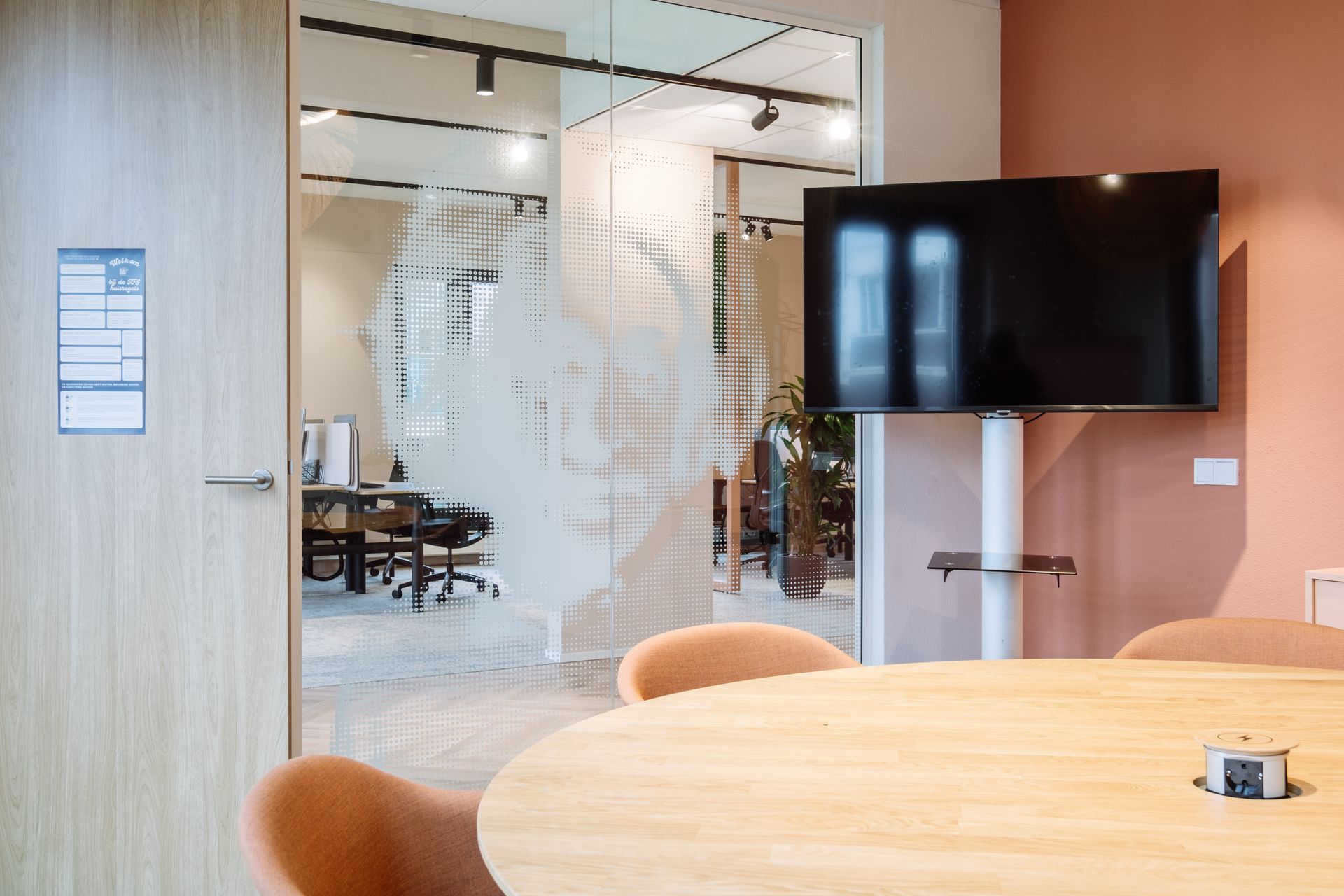 Modern conference room with glass walls, a round wooden table, and a wall-mounted TV.