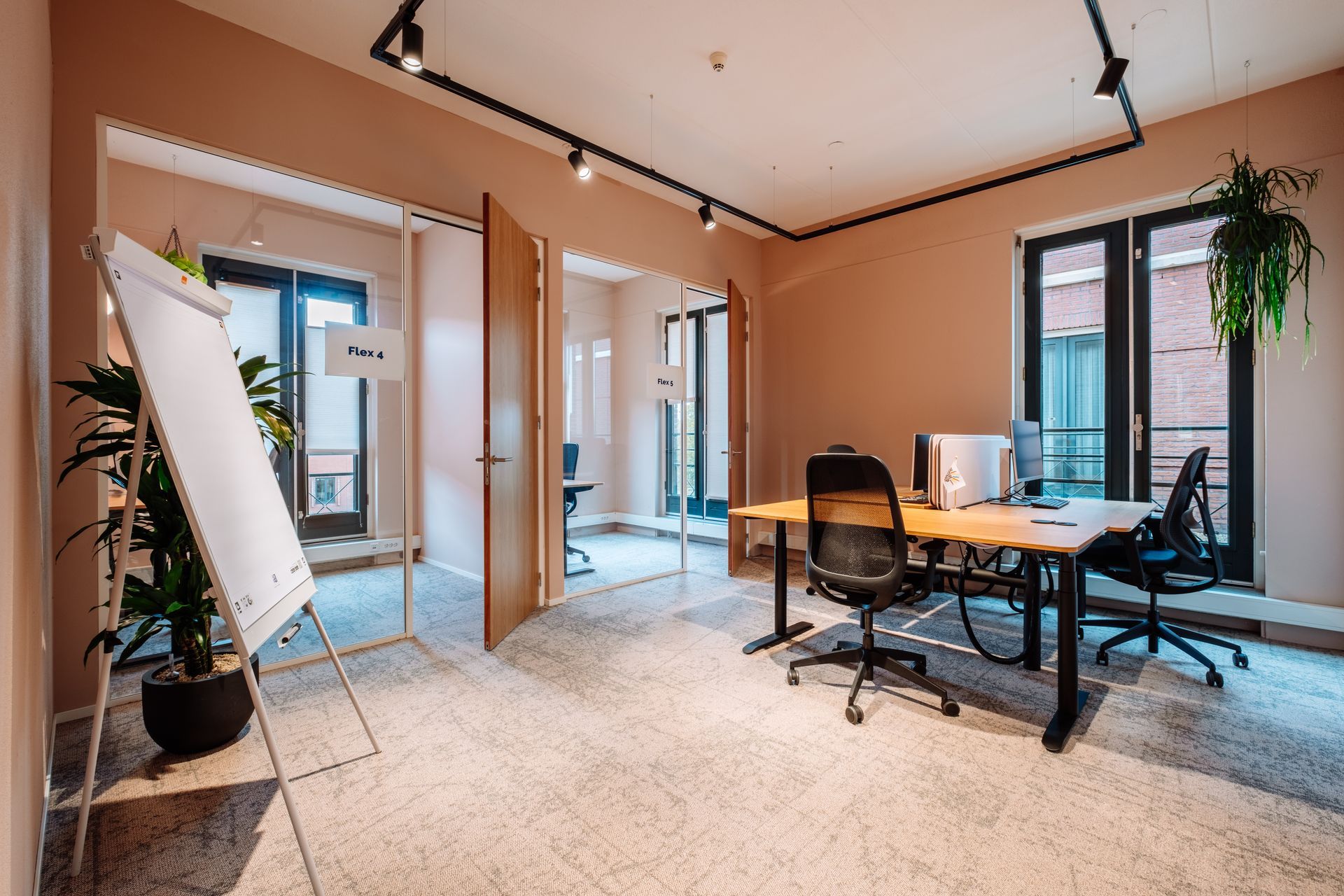 Modern office with desks, rolling chairs, whiteboard, and large windows in a bright peach-colored room