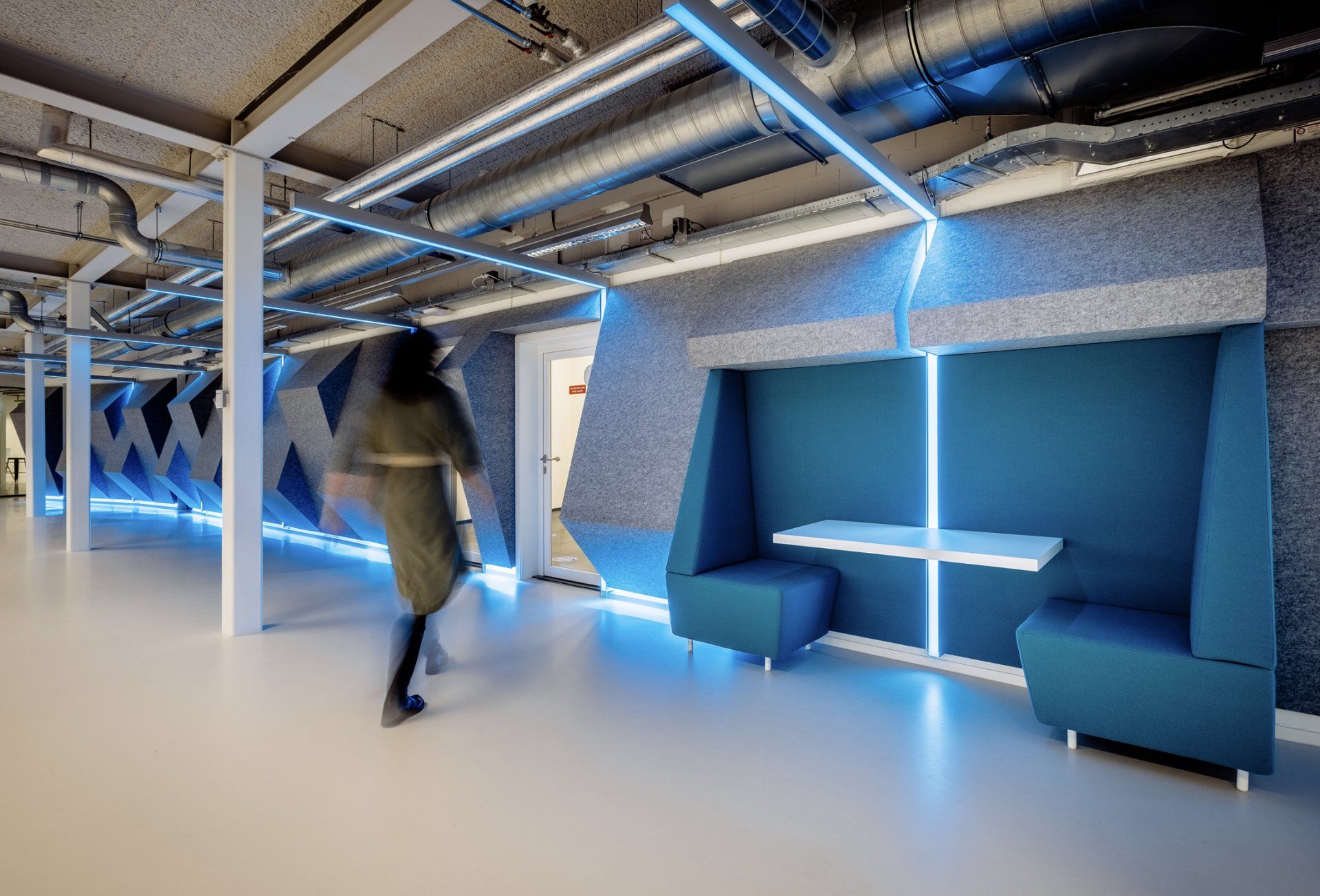 Na verbouwing Een modern vitale kantooromgeving met zichtbare leidingen, blauwe accentverlichting en geïntegreerde blauwe zitbanken in het nieuwe kantoor van Shypple in Rotterdam, interieurontwerp voor KuóStudio
