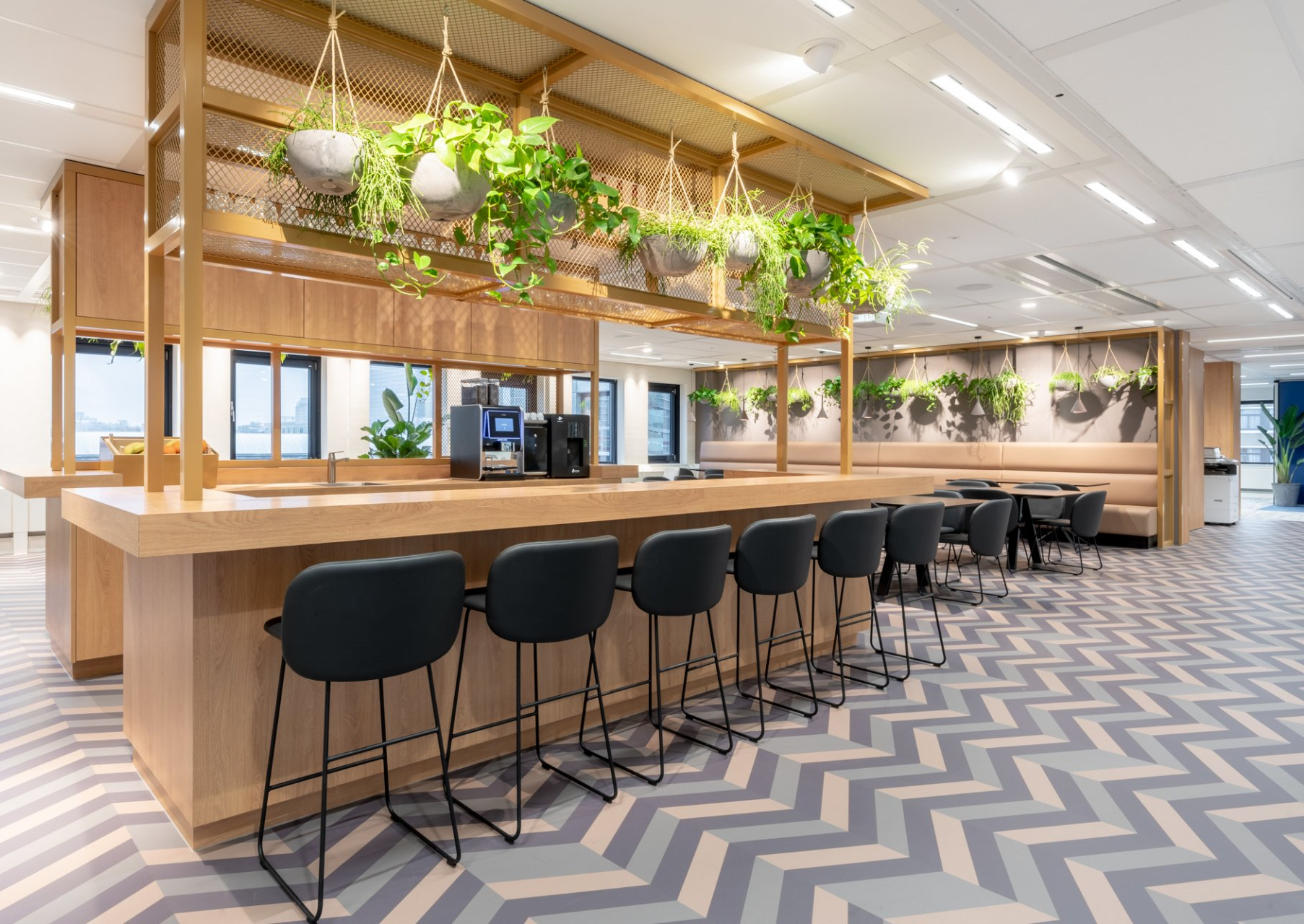 Moderne kantoorlounge met barkrukken, hangplanten en een vloer met visgraatpatroon.