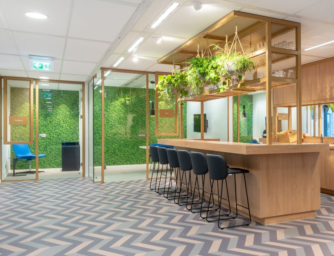 Moderne kantoorlounge met houten bar, zwarte barkrukken, groene plantenwand en zigzag vloer in Rijswijk