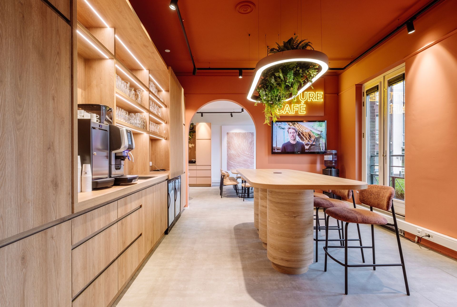 Na verbouwing: Het Future Café met houten kasten, terracotta muren, een kookeiland met barkrukken en een hangende plantenbak in het nieuwe kantoor van The Future Group Interieurontwerp KuóStudio