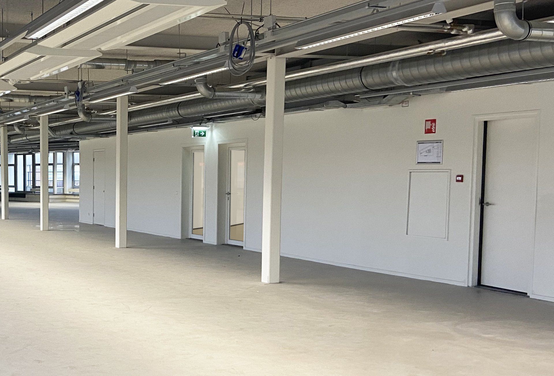 Voor verbouwing: Een lichte, moderne kantoorhal met witte muren, witte steunpilaren, zichtbare plafondleidingen in het kantoor van Shypple in Rotterdam.