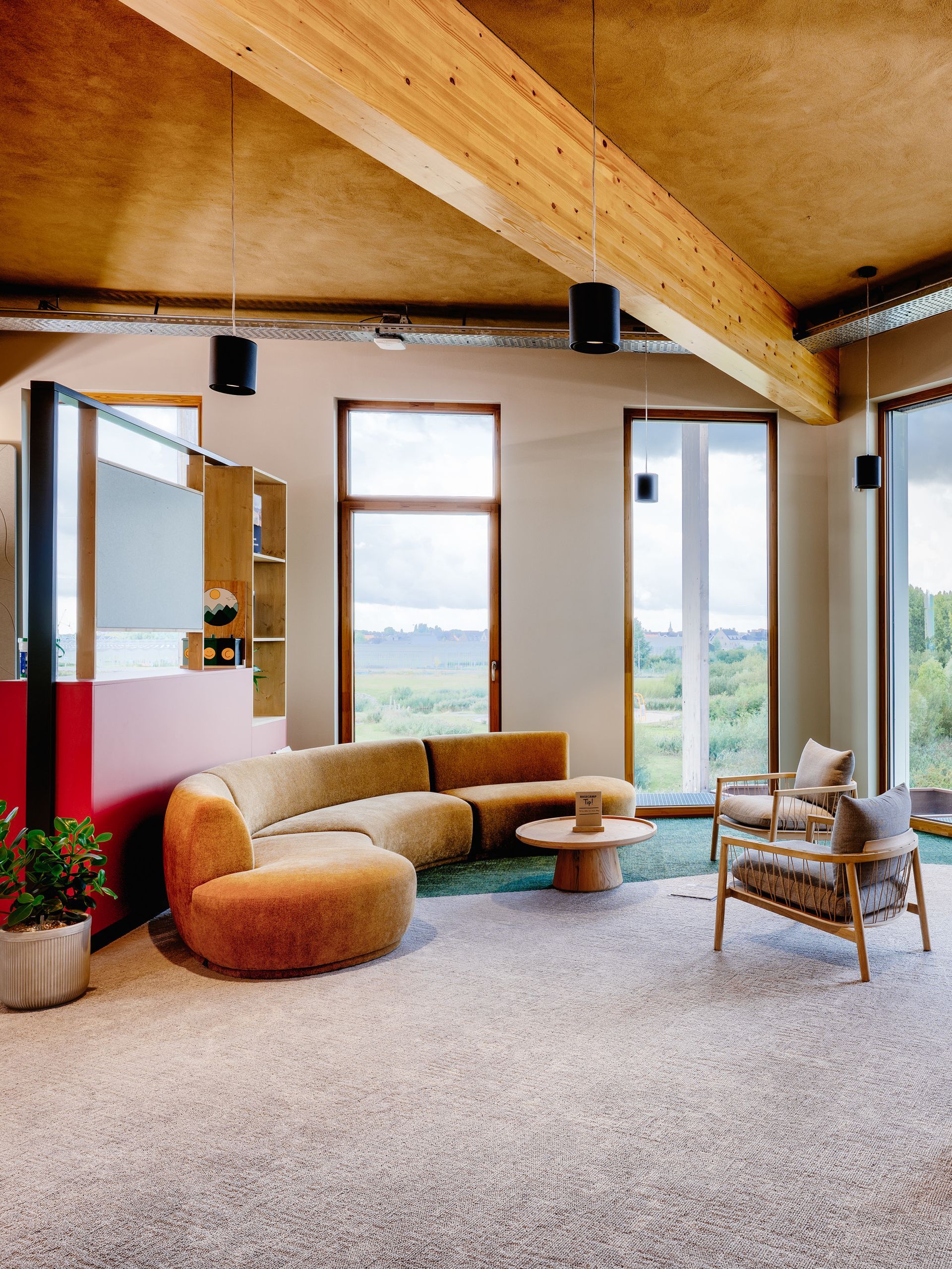 Lichte kantoor met beige bank, ronde fauteuil, houten balken en grote ramen met uitzicht.