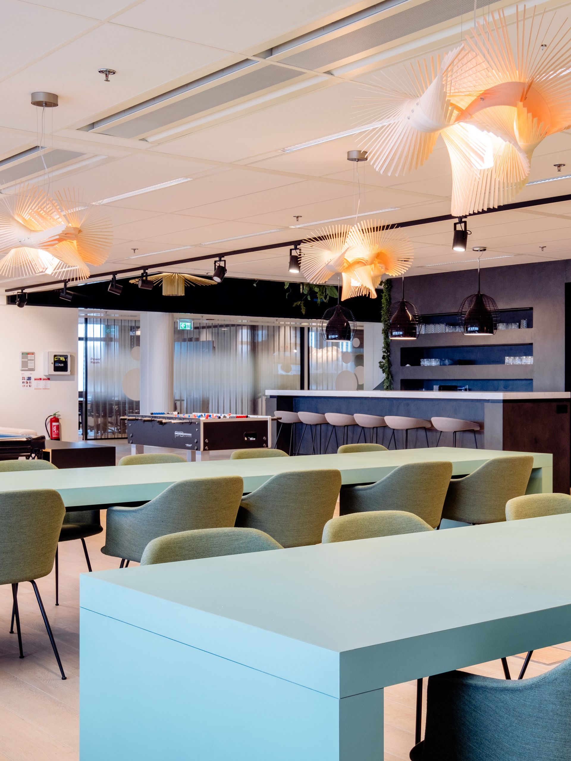 Modern lounge interior with pastel tables, green chairs, and hanging pendant lights
