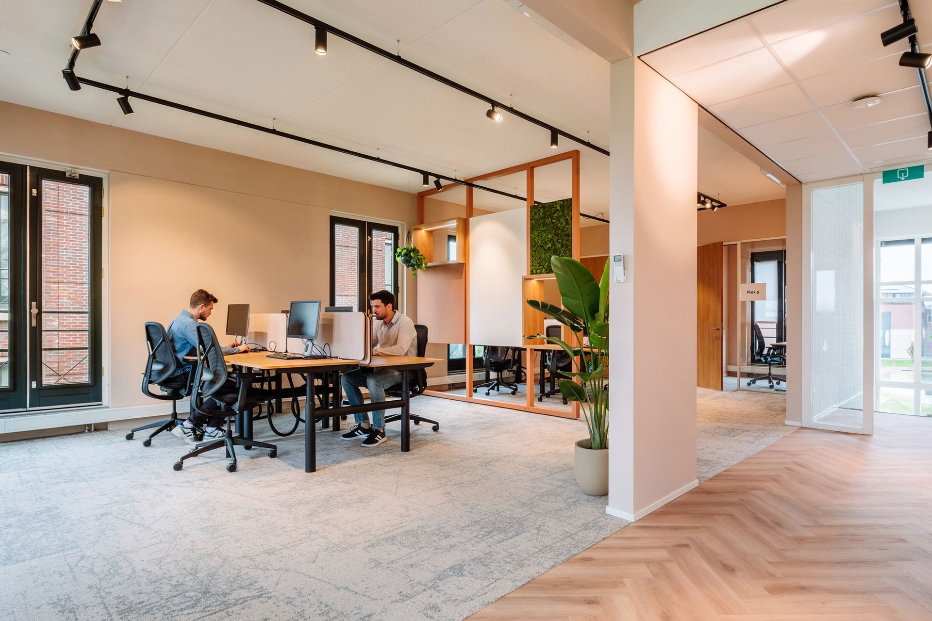 Een modern, open kantoor met neutrale muren, een visgraatparketvloer en ergonomische stoelen aan houten bureaus in het nieuwe kantoor van The Future Group Interieurontwerp KuóStudio