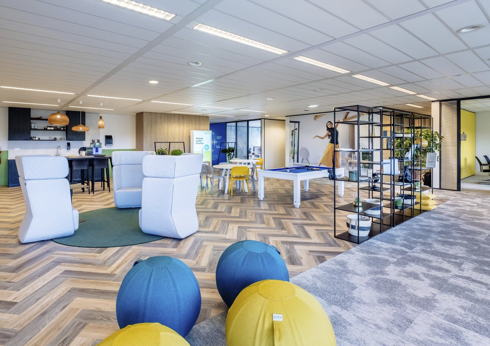 Moderne kantoorlounge met tafels, stoelen, krukken, planken en kleurrijke zitzakken op een vloer met patroon.