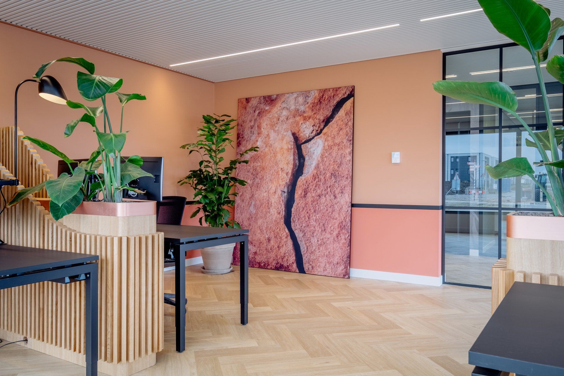 Het moderne kantoorruimte is voorzien van terra kleurige muren, een visgraatparketvloer, planten en abstracte muurkunst. in het nieuwe kantoor van EBH Legal in Naaldwijk, interieurontwerp door KuóStudio