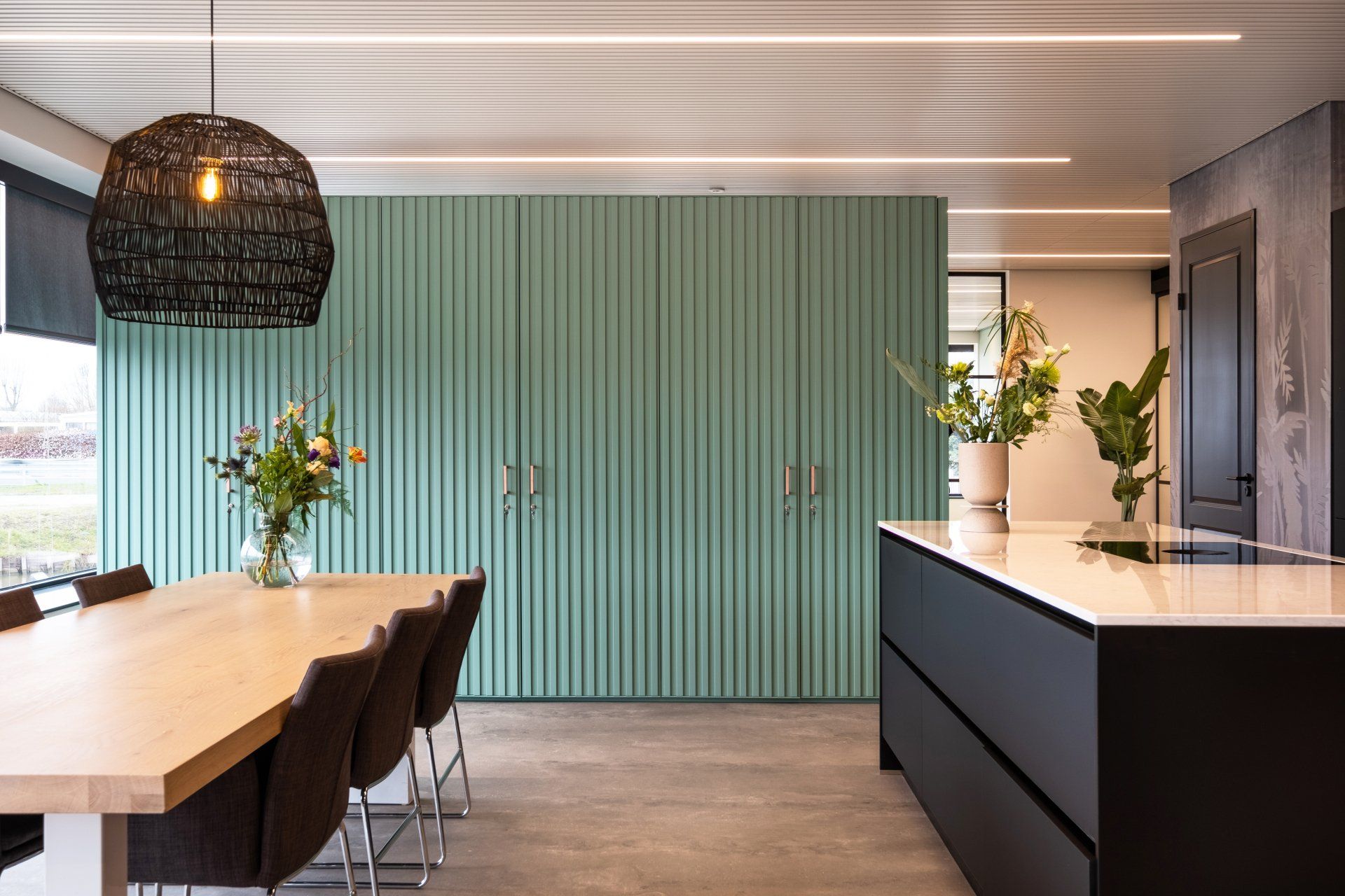 Een moderne keuken met een lichte houten tafel, donkere stoelen, een mintgroene lattenwand en een zwart keukeneiland van EBH Legal in Naadwijk, interieurontwerp door KuóStudio