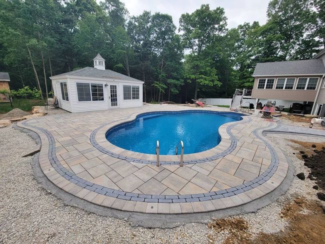 A large swimming pool is surrounded by trees and a wooden deck. A large swimming pool is surrounded by trees and a wooden deck.