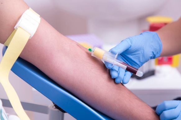 Gloved clinician drawing blood from a patient’s arm with a syringe in a medical setting