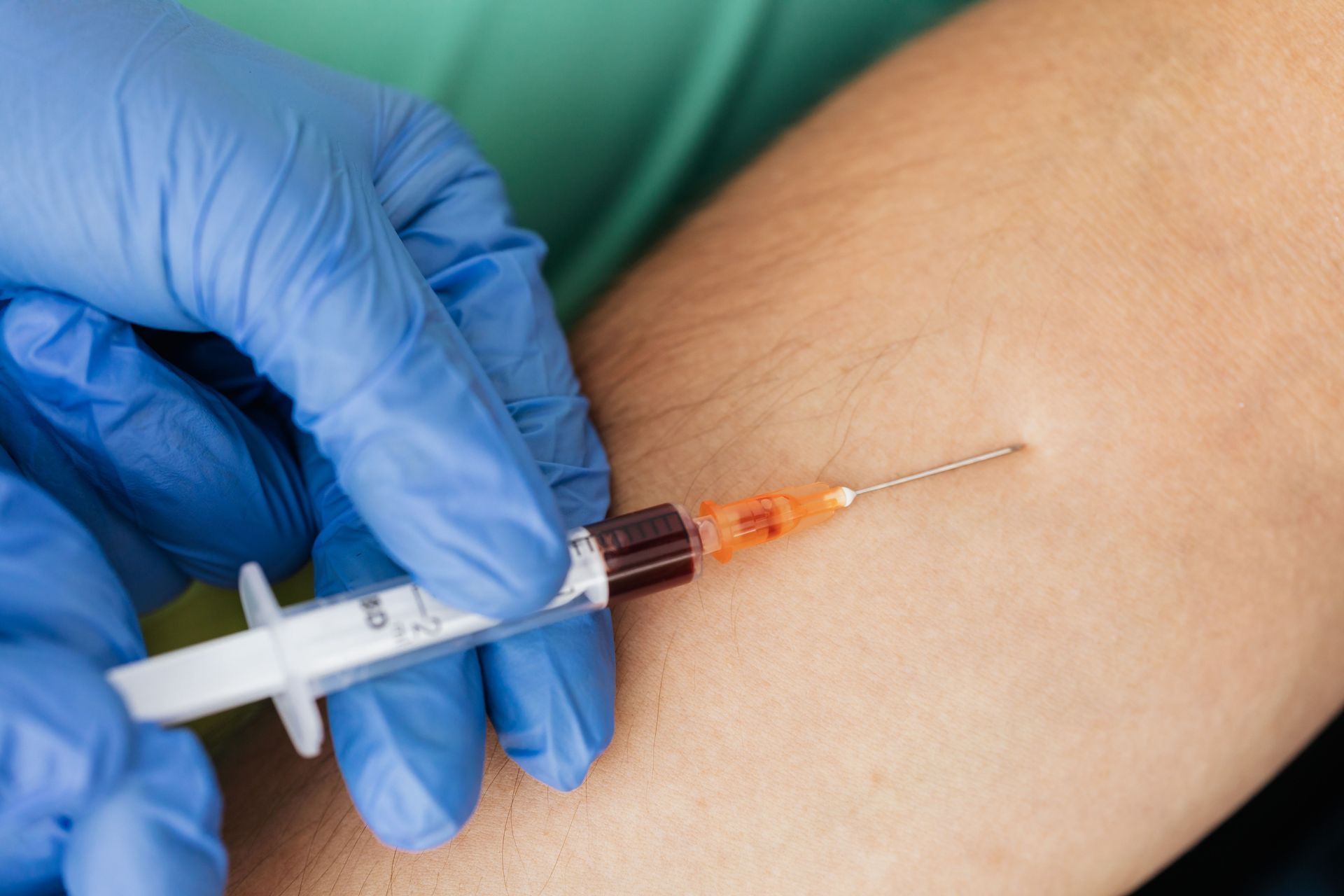Gloved hand giving a syringe injection into an arm