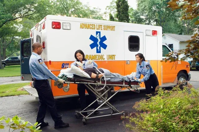 Paramedics loading a patient into an orange-and-white ambulance on a suburban street