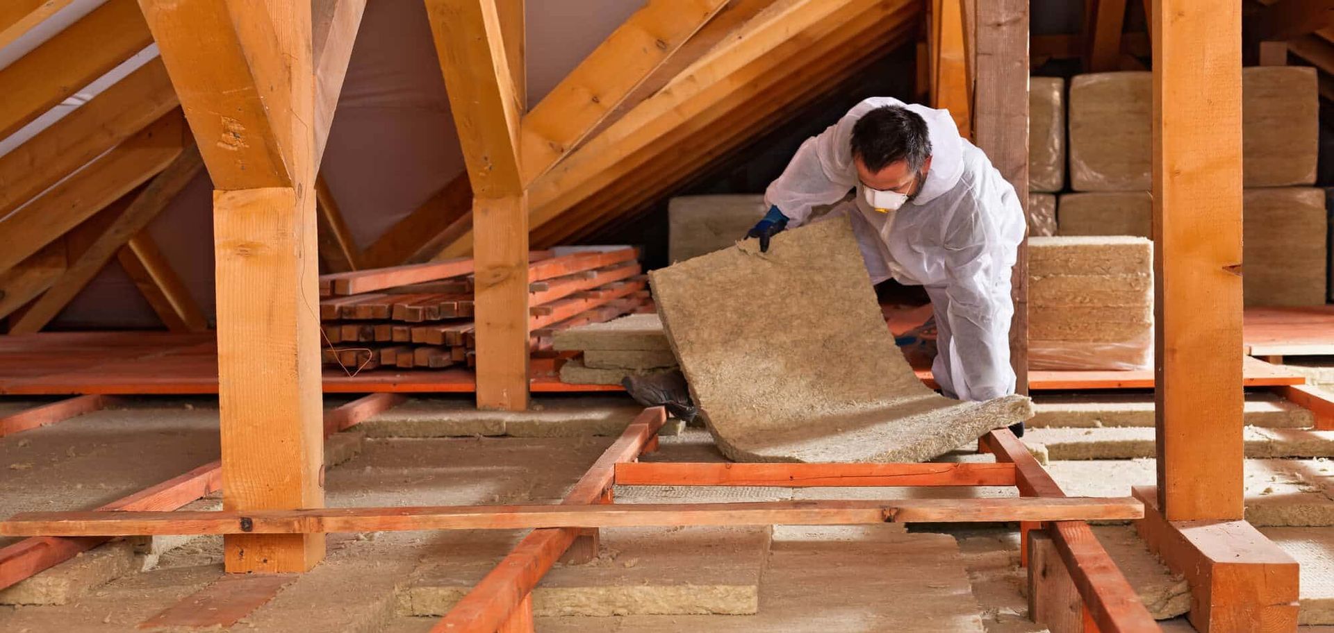 Worker installing insulation in an attic with exposed wooden beams