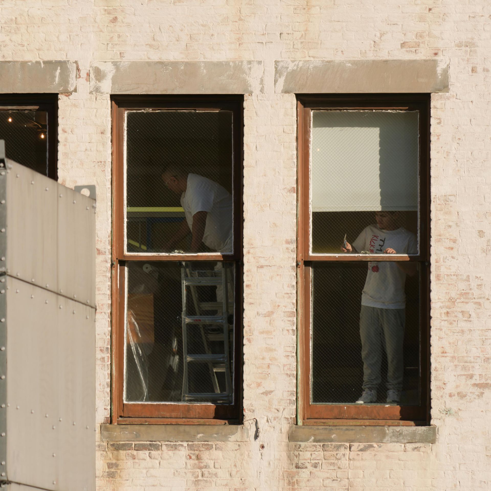 Two workers visible through tall windows, one on a ladder, in a beige building facade