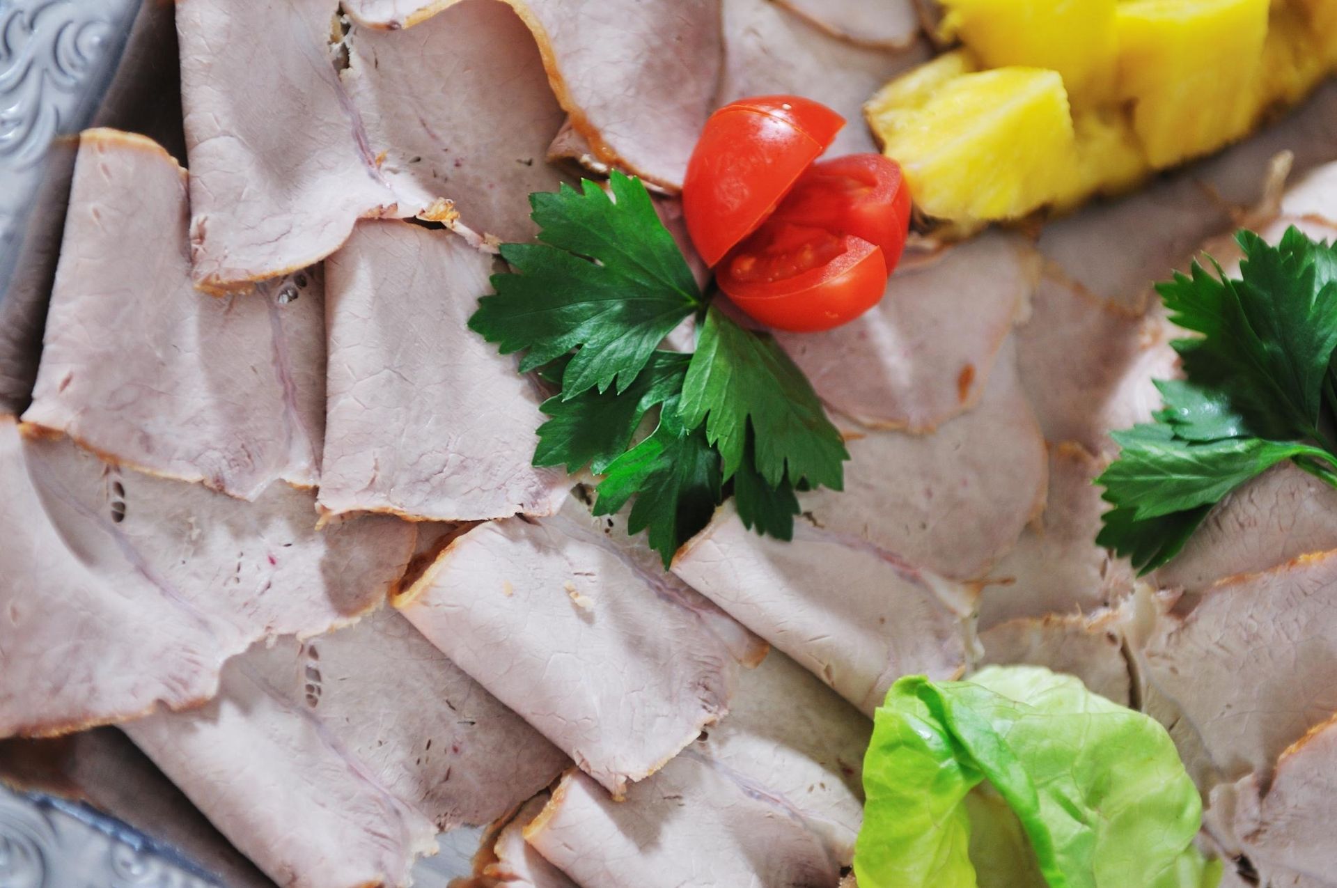 Thinly sliced deli meat with parsley, cherry tomatoes, pineapple, and lettuce on a platter